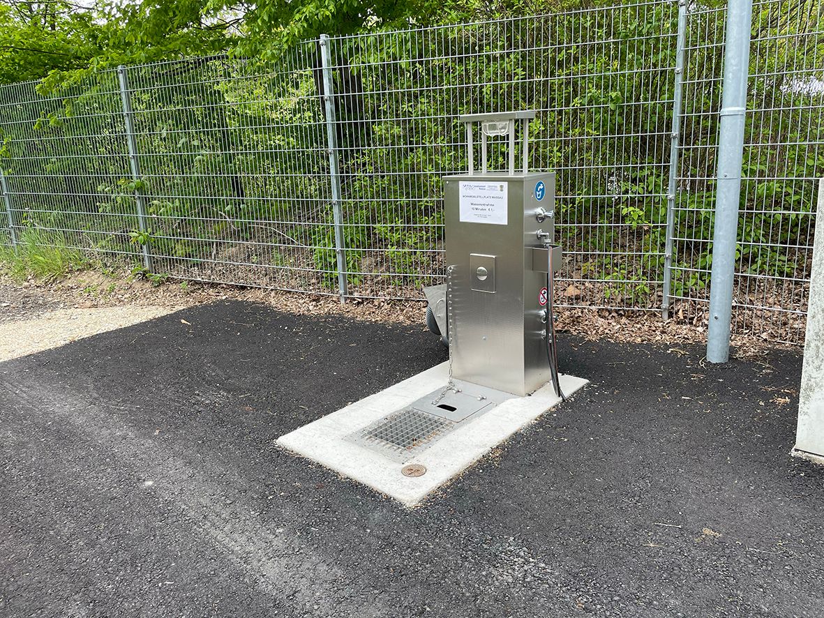 Kovová vodovodní stanice vedle plotu na asfaltu.