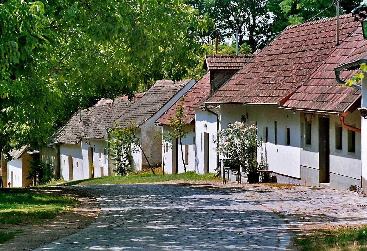 Eine gepflasterte Straße führt an einer Reihe traditioneller weißer Häuser mit roten Dächern vorbei, umgeben von grünen Bäumen.