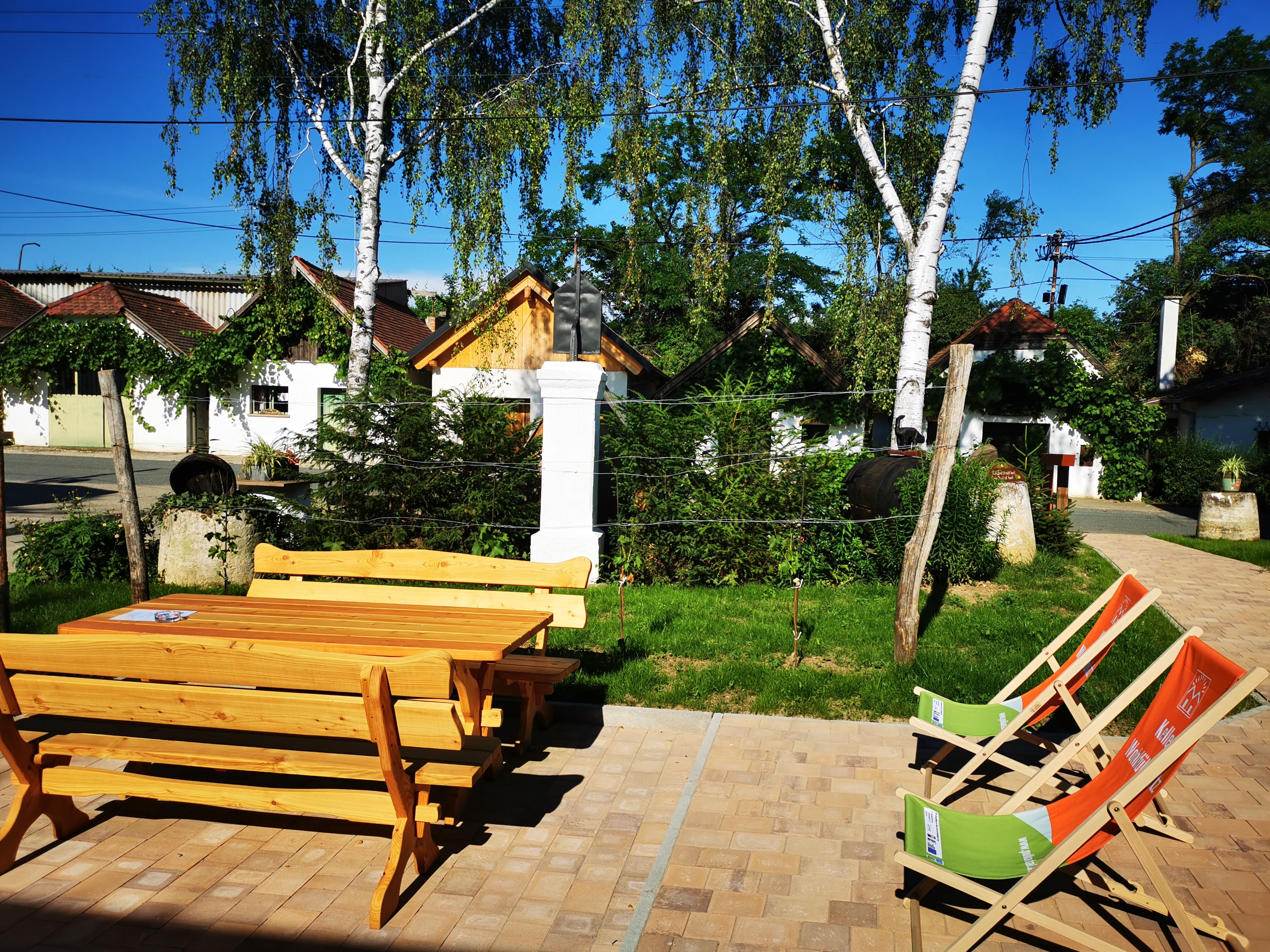 Wooden table and chairs outside with deckchairs, surrounded by trees and small buildings in Hadres.