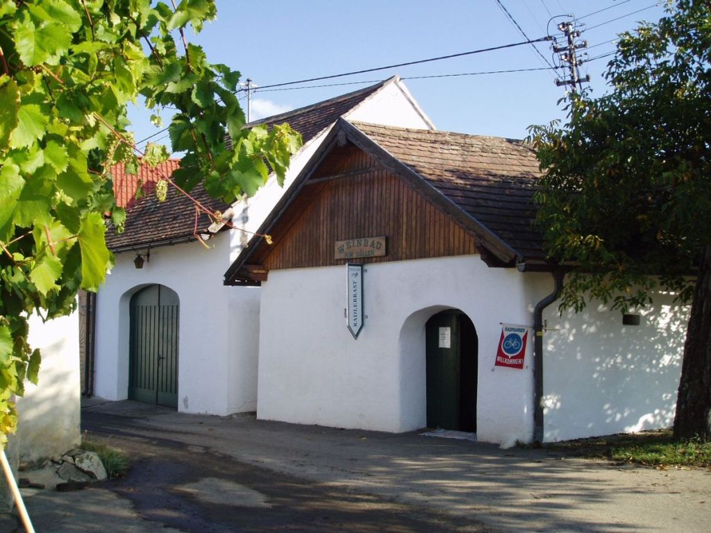 Weißes Gebäude mit Holzdach, Weinreben im Vordergrund.