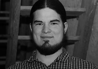 Portrait of a young man with a beard and long hair, wearing a checked shirt.