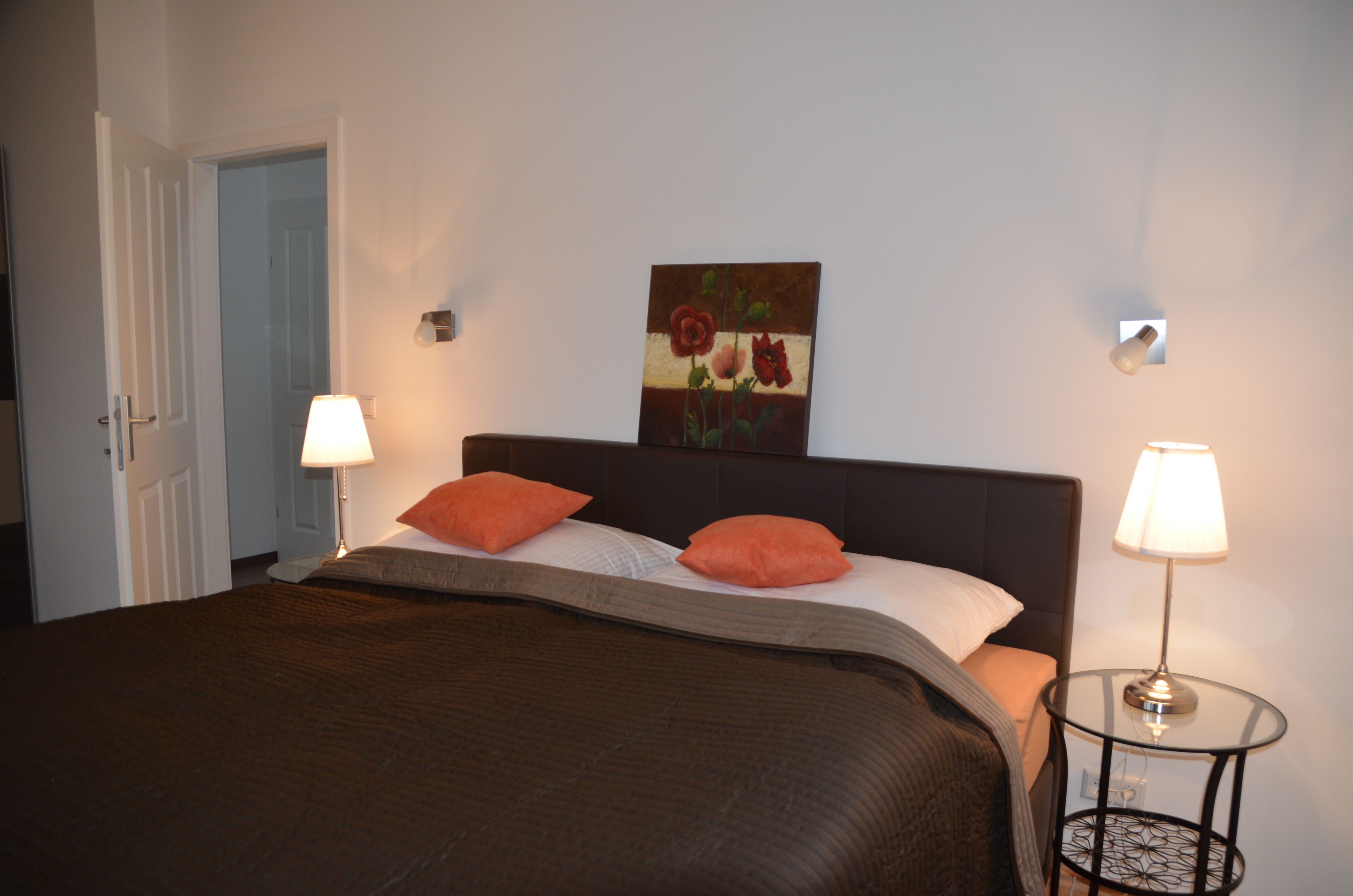 Bedroom with double bed, two bedside lamps and a painting on the wall.