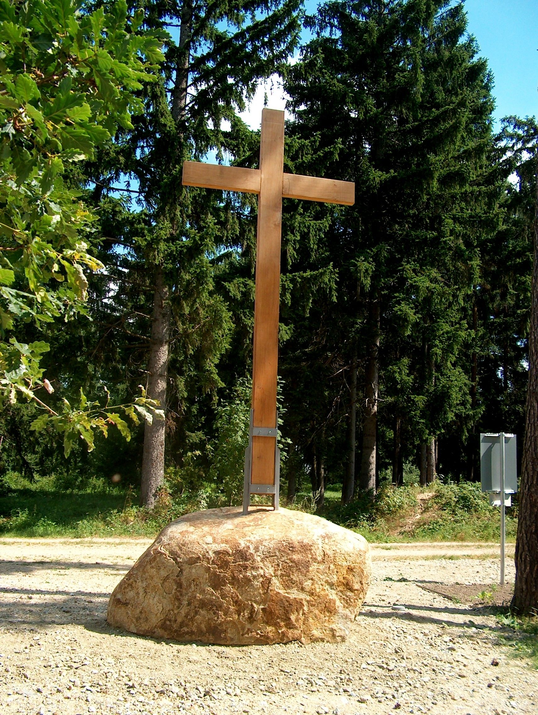 Ein hölzernes Gipfelkreuz auf einem großen Felsen, umgeben von hohen Tannenbäumen.