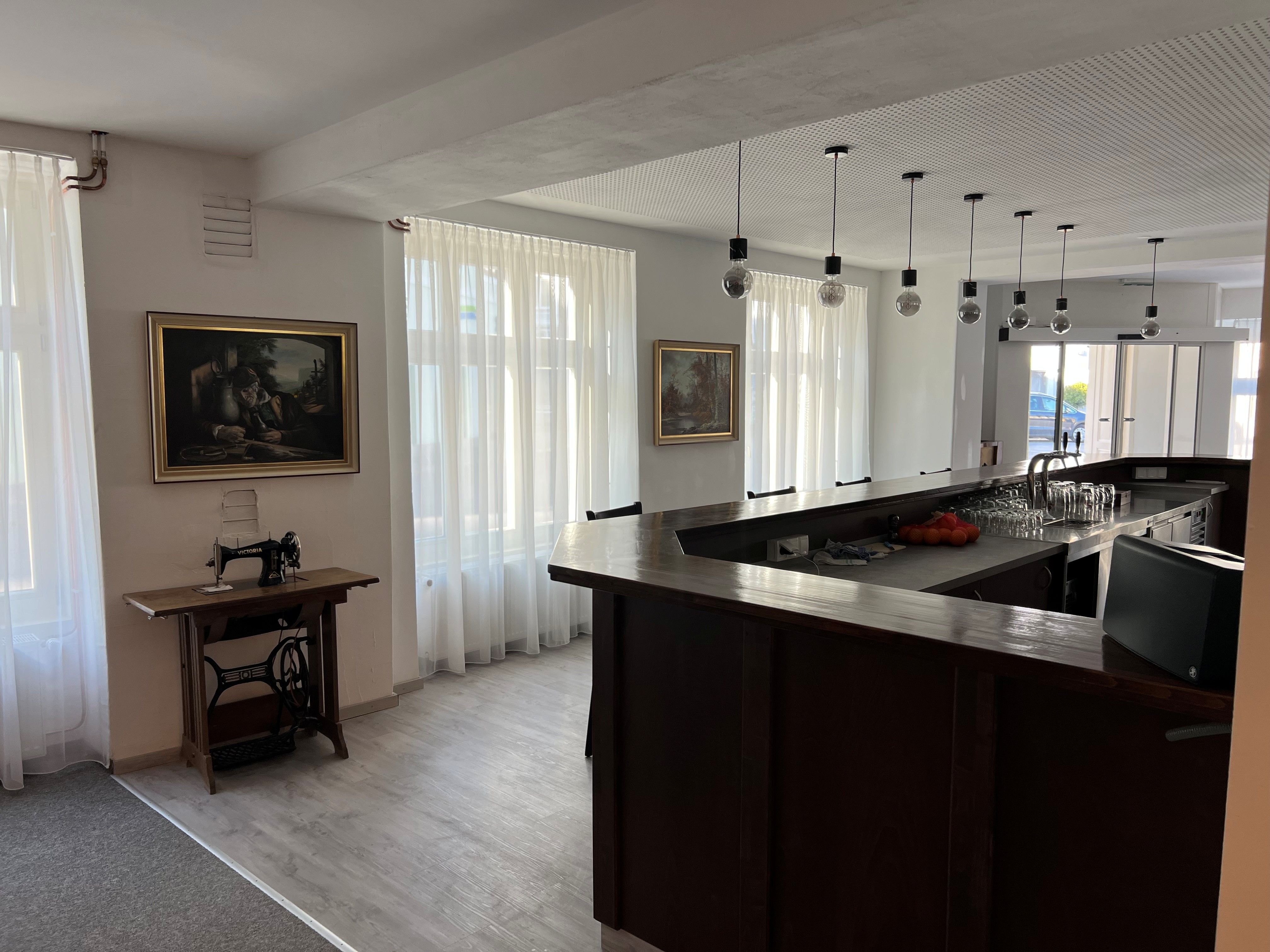 Ein moderner Barbereich mit dunkler Holztheke, hängenden Glühbirnen und einer alten Nähmaschine auf einem Tisch.