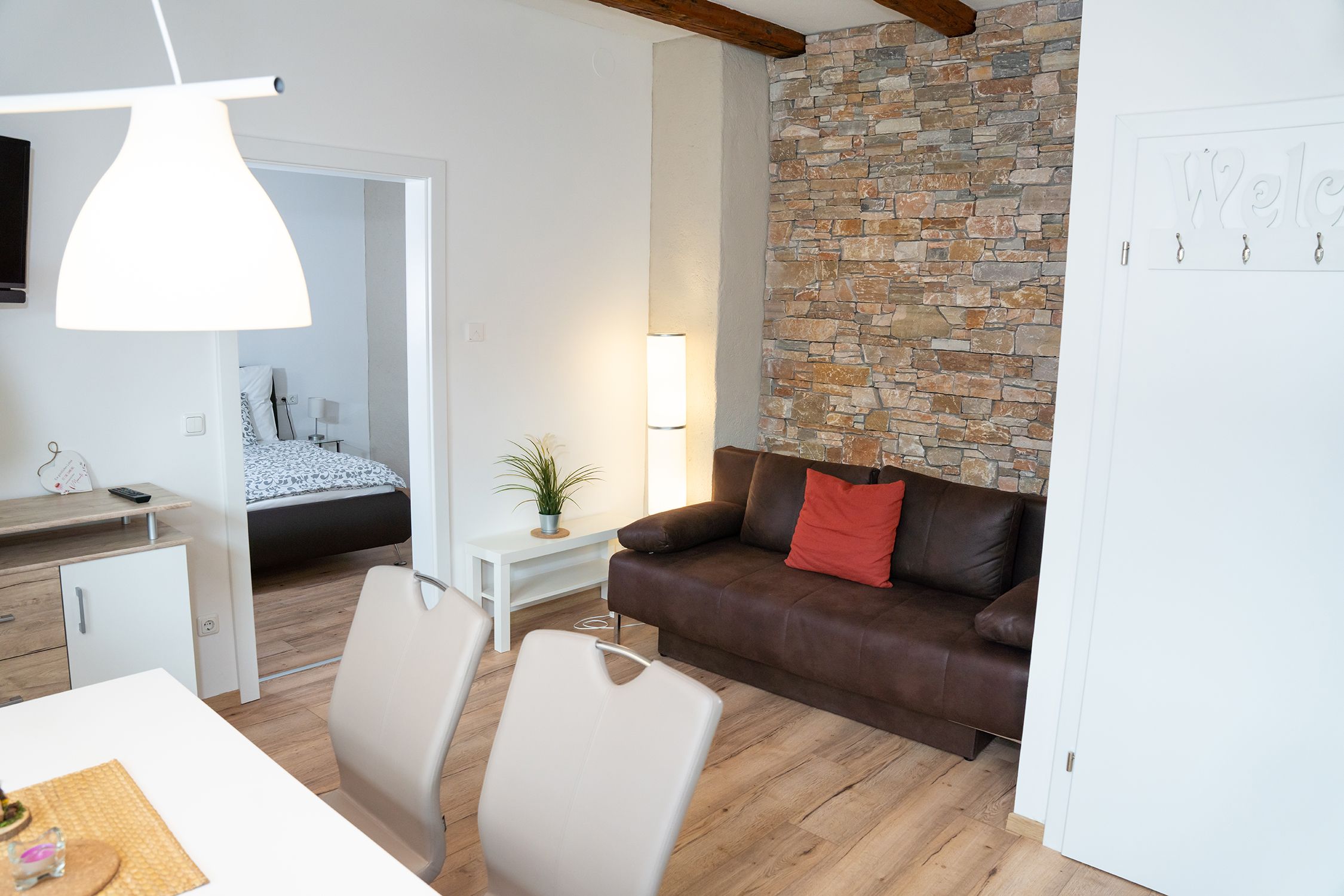 Modernes Wohnzimmer mit braunem Sofa, Steinwand und Blick ins Schlafzimmer.