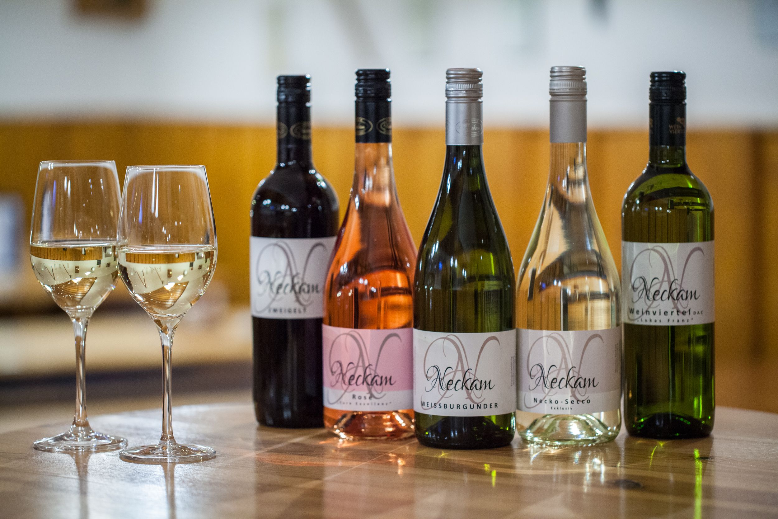 Fünf Weinflaschen und zwei gefüllte Weingläser auf einem Holztisch.