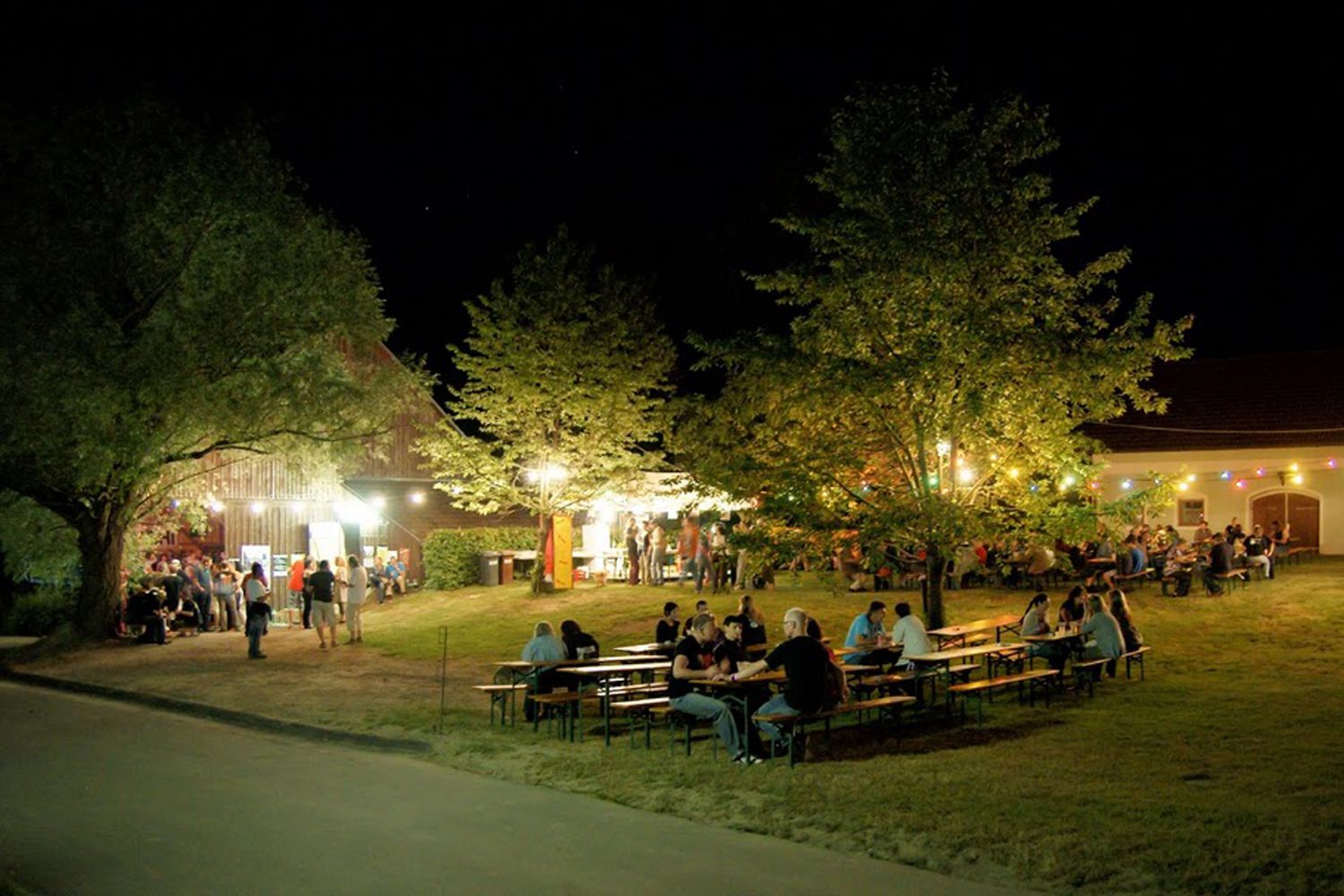 Nachtaufnahme eines beleuchteten Veranstaltungsbereichs im Freien mit Menschen an Tischen und bunten Lichtern.