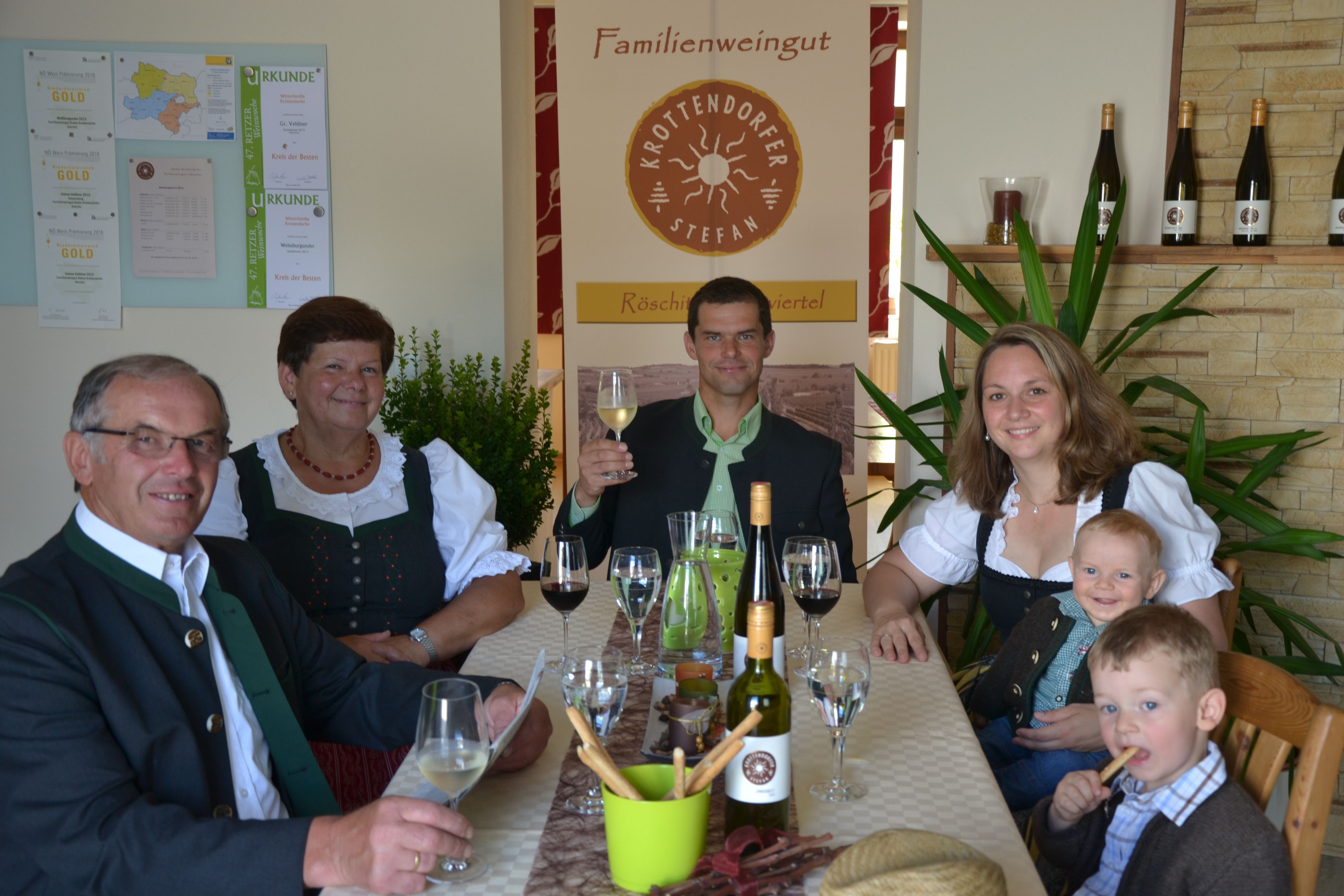 Familie in traditioneller Kleidung sitzt an einem Tisch mit Wein und Gläsern.