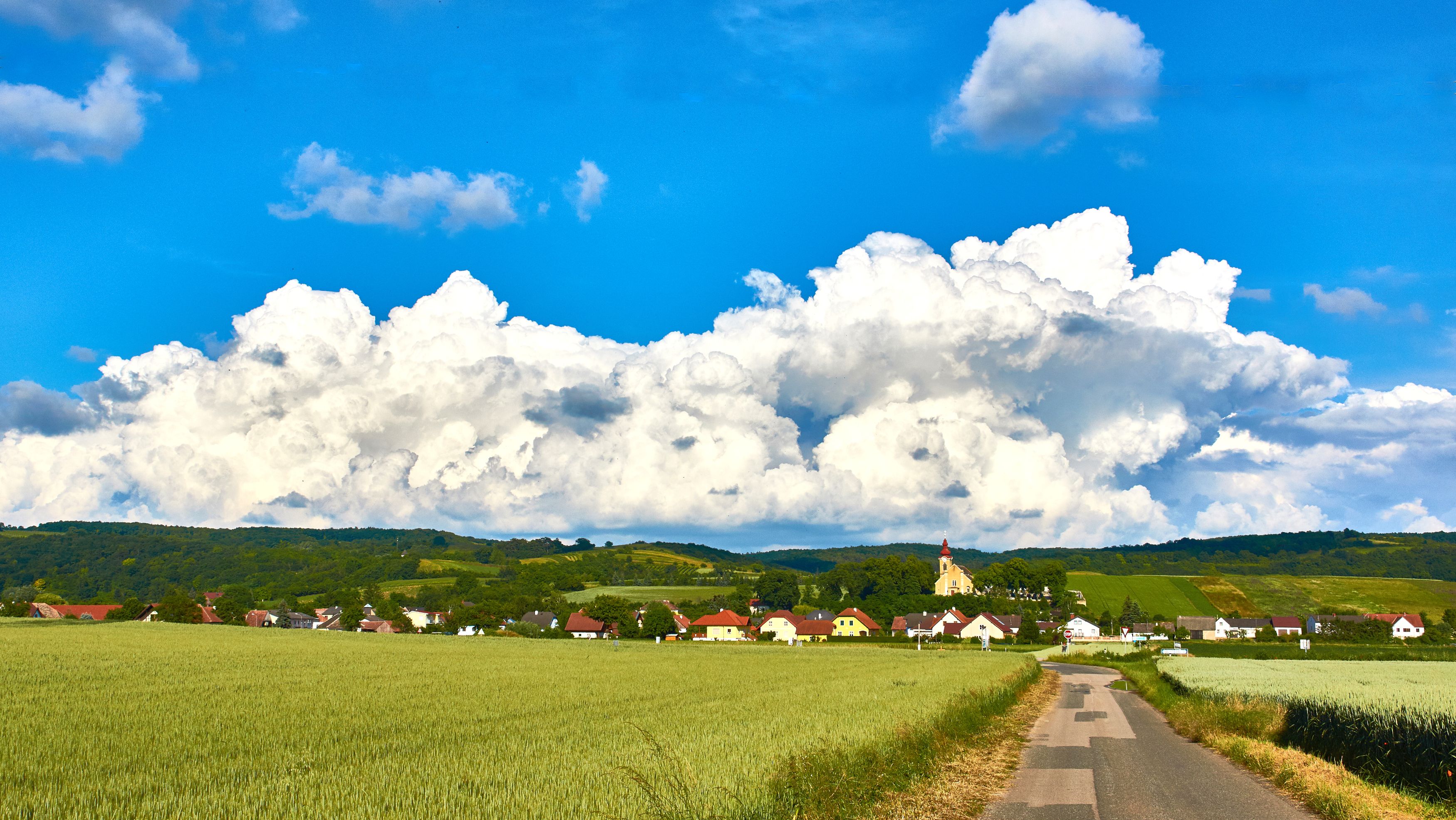 Landschaft mit Dorf, Feldern und Kirche vor großen Wolken.