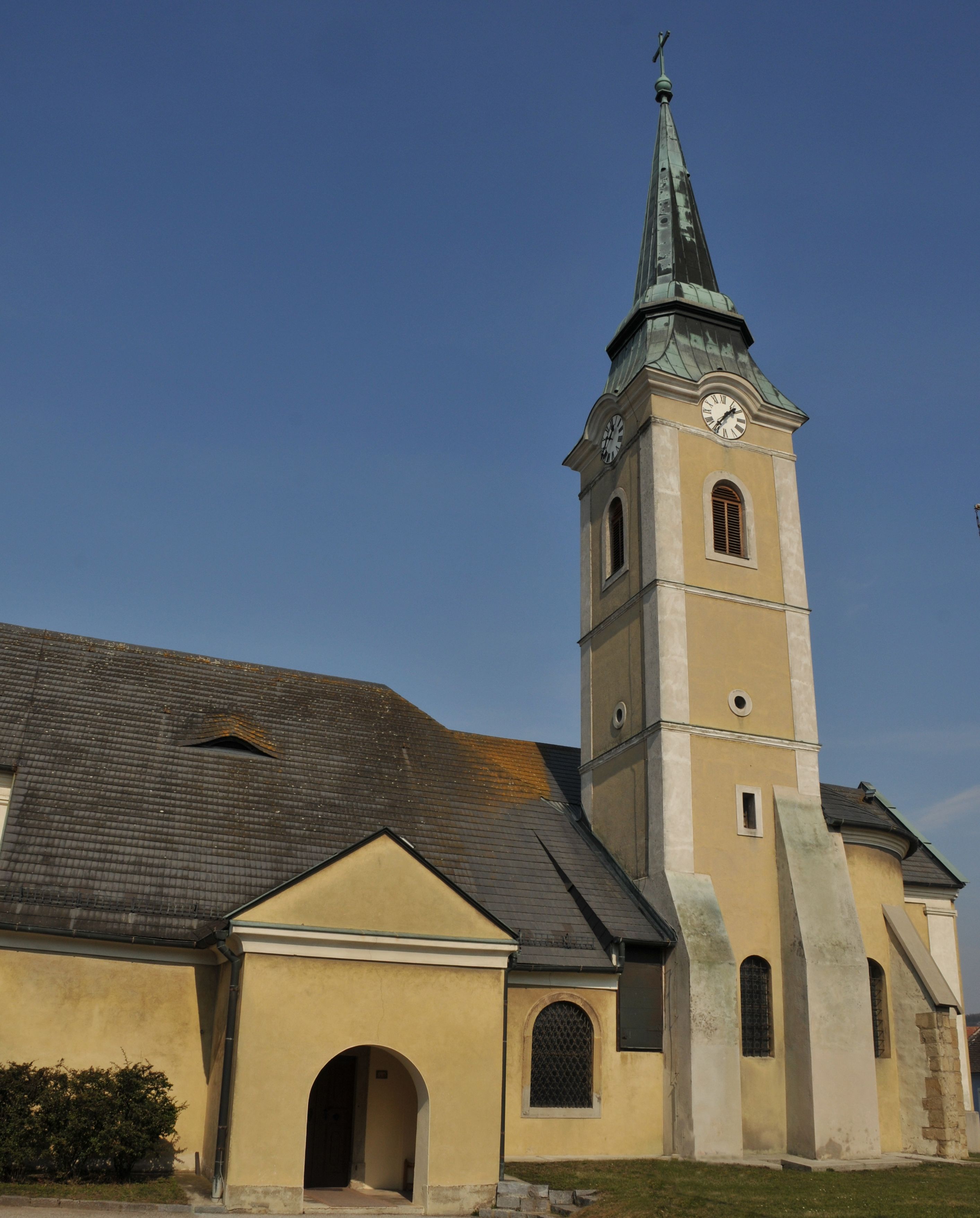Church in Leitzersdorf with clock tower and pointed roof against a blue sky.