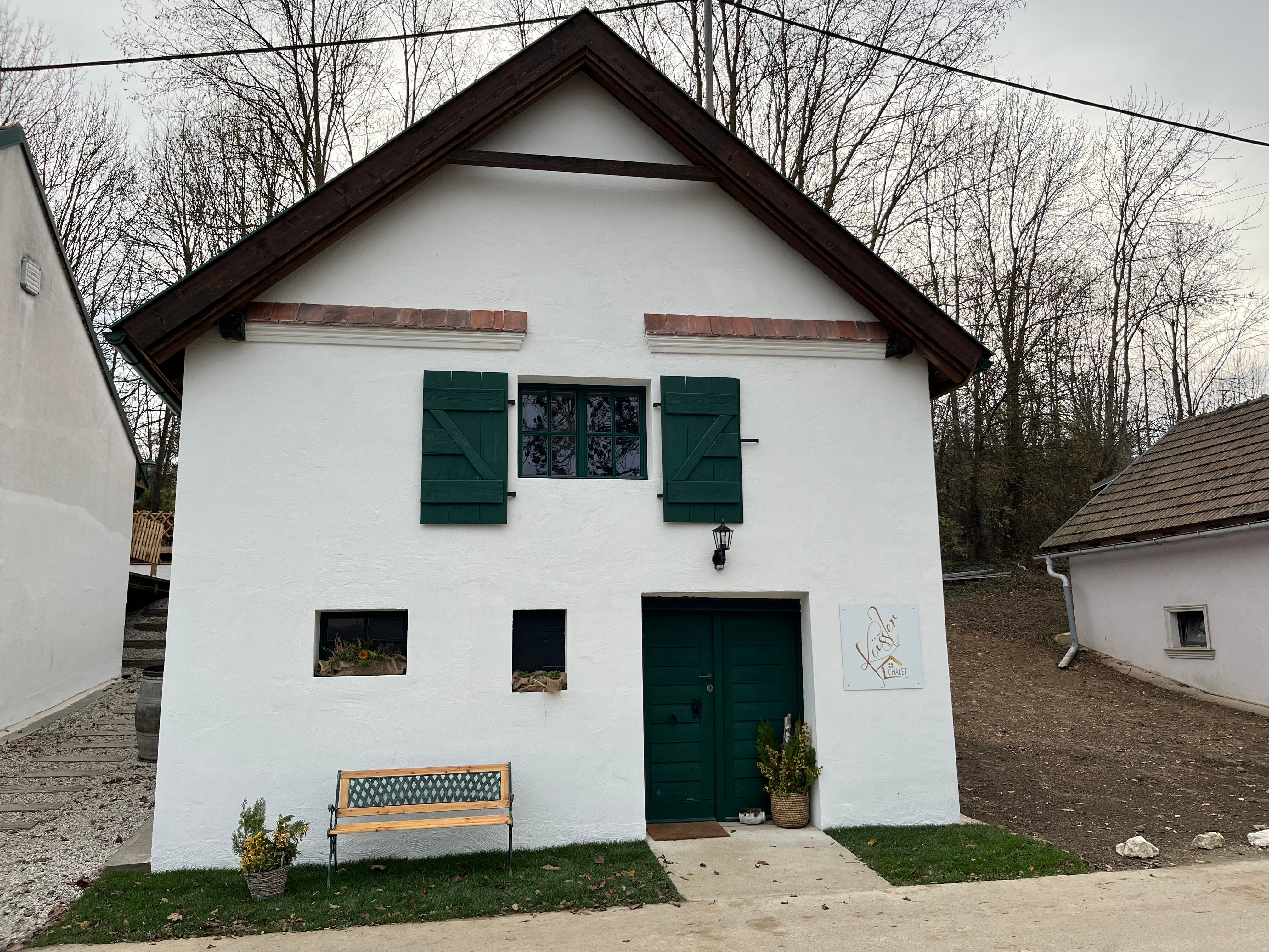 Fassade des Winzerhofs Küssler mit weißem Putz, grünen Fensterläden und Eingang, davor eine Bank und Pflanzkübel.