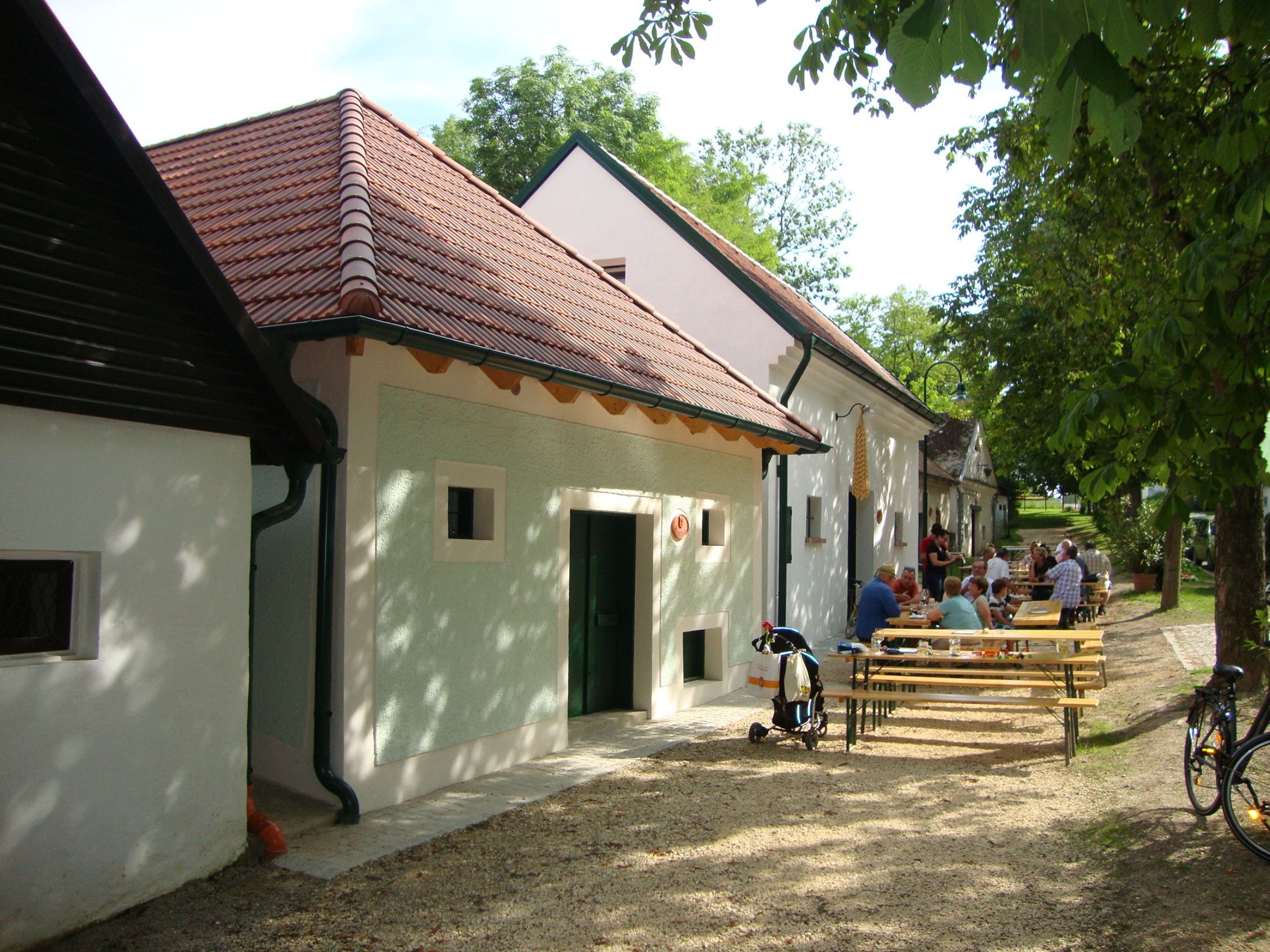 People sit at tables in front of traditional buildings with red roofs.