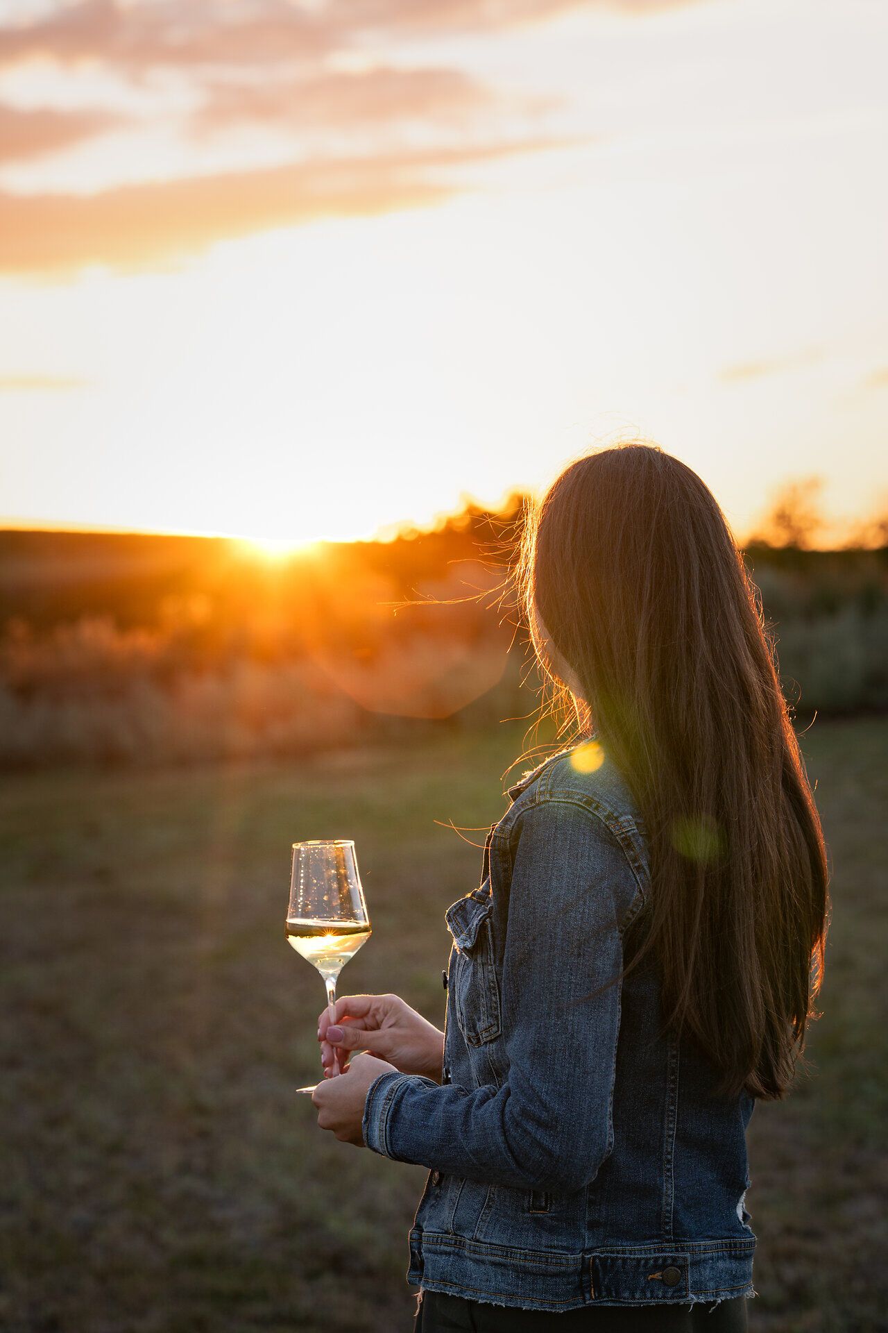 Eine Frau genießt mit einem Glas Weißwein in der Hand den Blick auf den Sonnenuntergang.