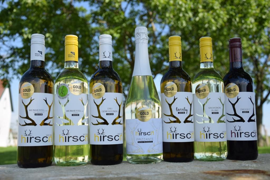 Sechs Weinflaschen der Marke Hirsch auf einem Tisch im Freien.