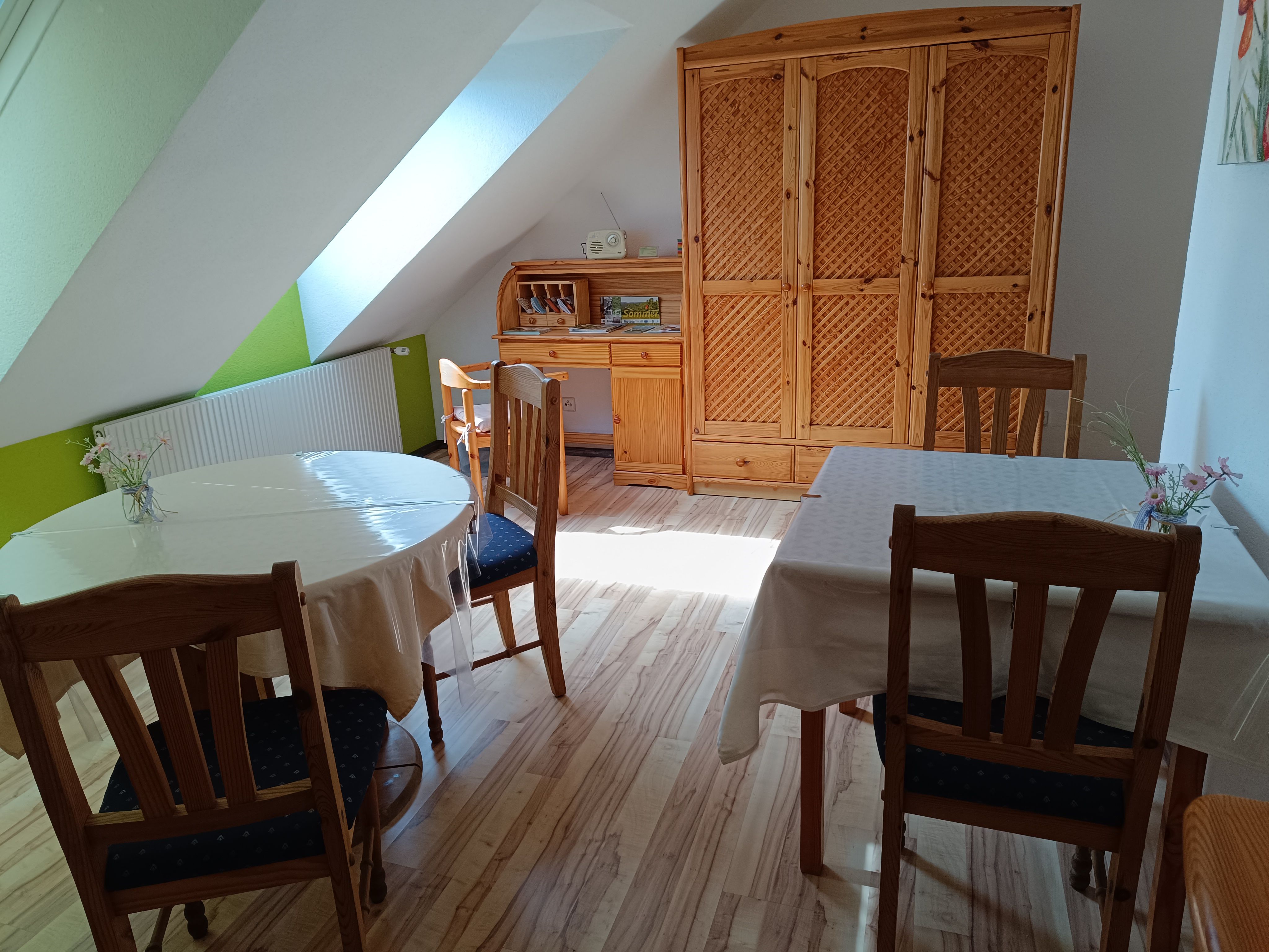 Ein gemütlicher Frühstücksraum mit Holzmöbeln, zwei gedeckten Tischen und einem Schrank unter einer Dachschräge.