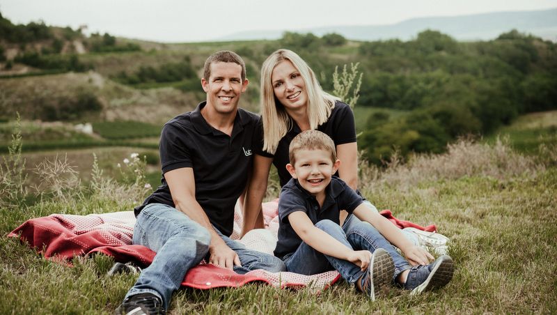 Family sitting on a blanket outdoors with a green landscape in the background.