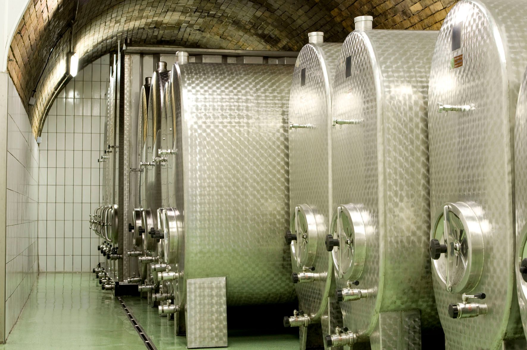 Stainless steel tanks in a wine cellar with a vaulted ceiling.