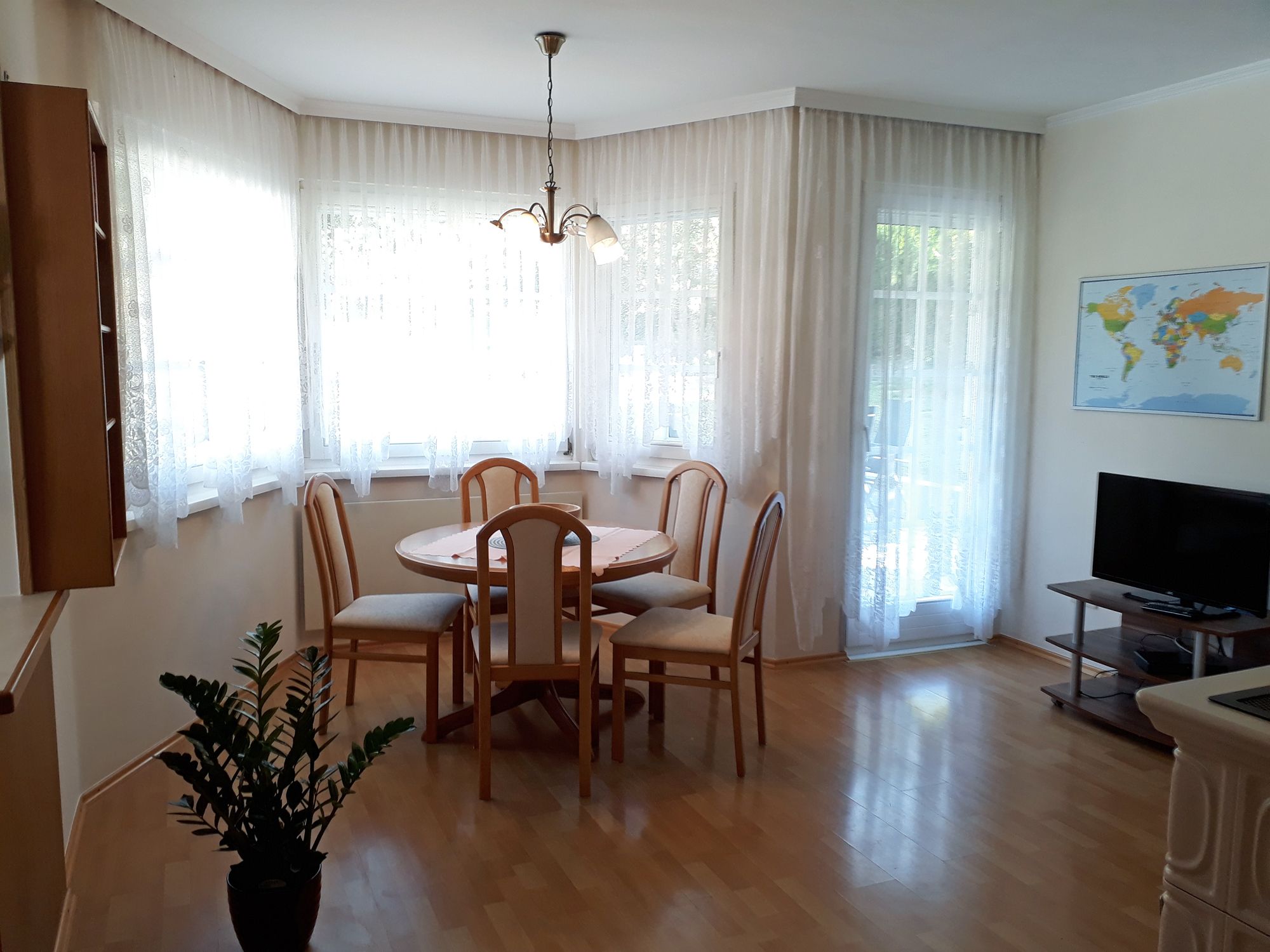 Helle Wohnküche mit Esstisch, Stühlen, TV und Weltkarte an der Wand.