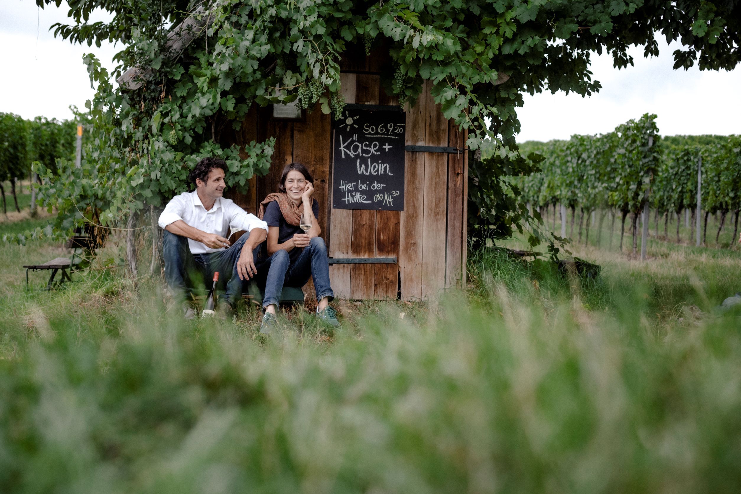 Two people are sitting in front of a wine hut in a vineyard.