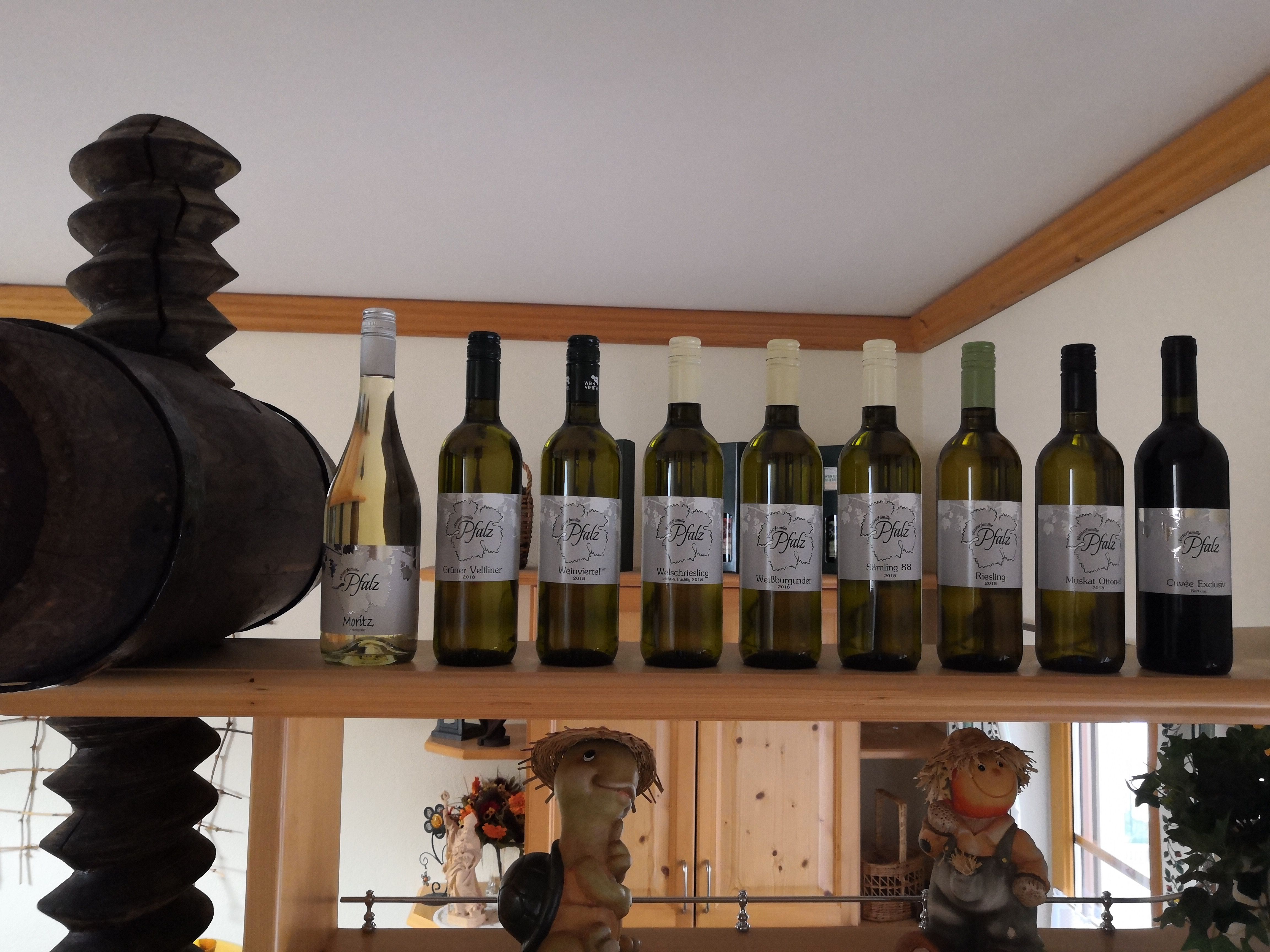 Wine bottles on a shelf with a wooden barrel and decorative figures.