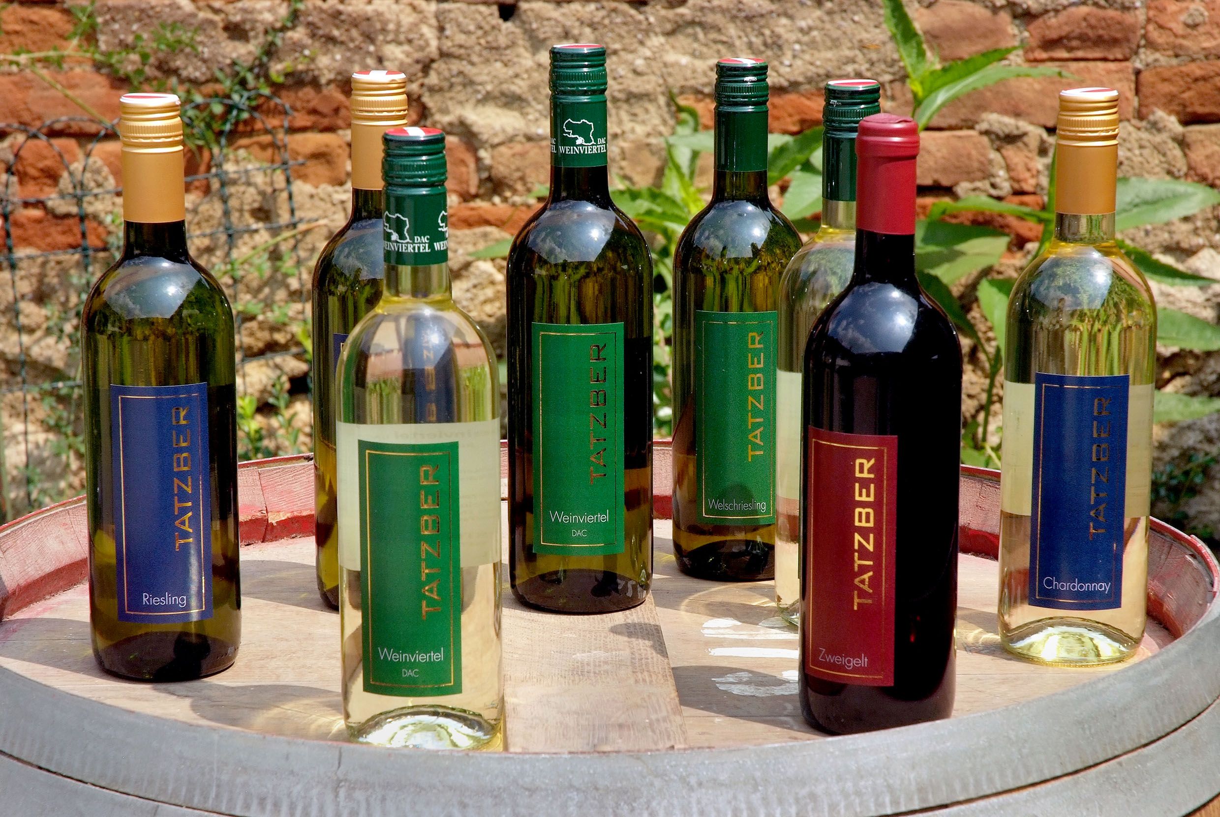 Various Tatzber wine bottles on a barrel in the open air.