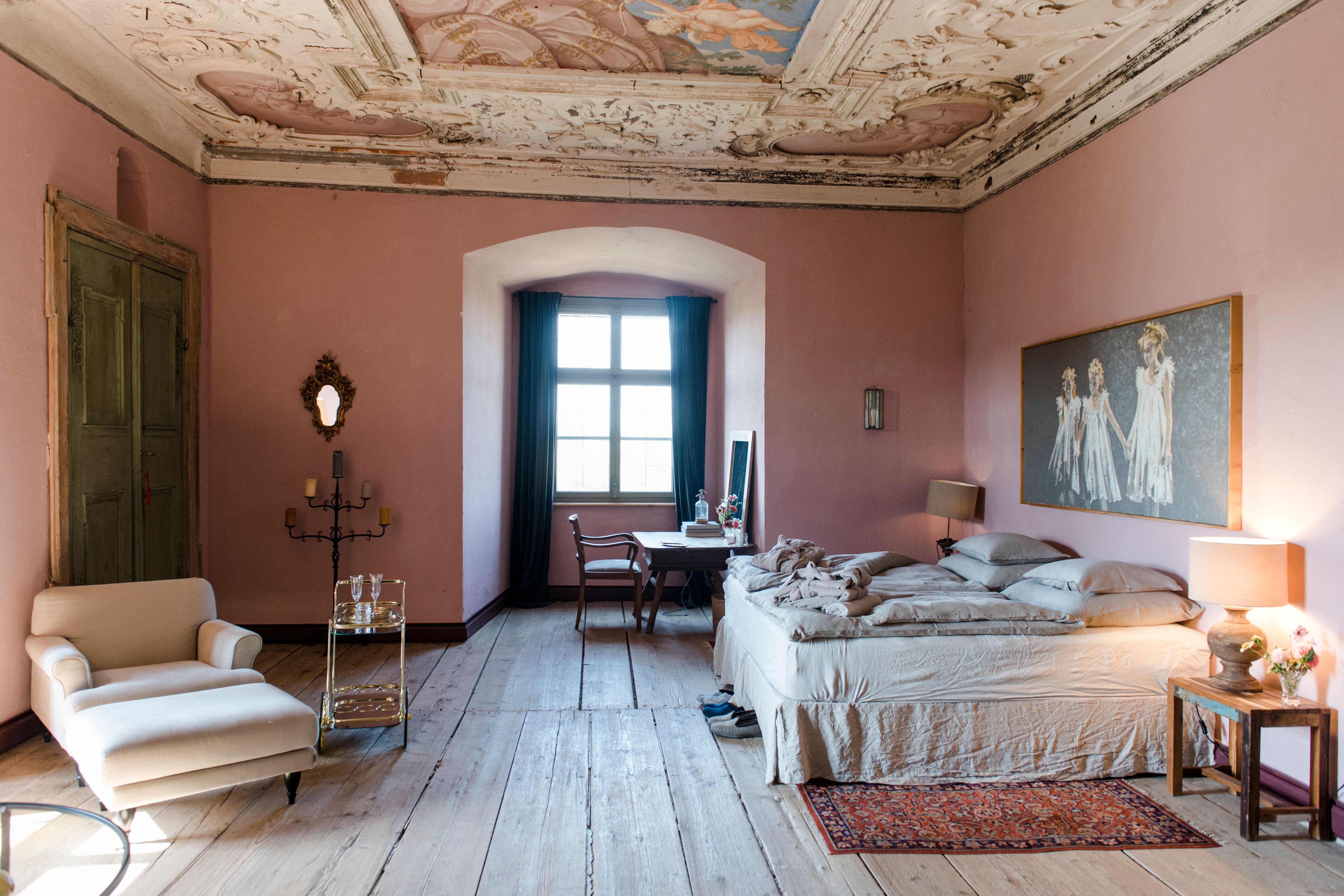 Elegantes Schlafzimmer mit antiker Decke, rosa Wänden und Holzboden.