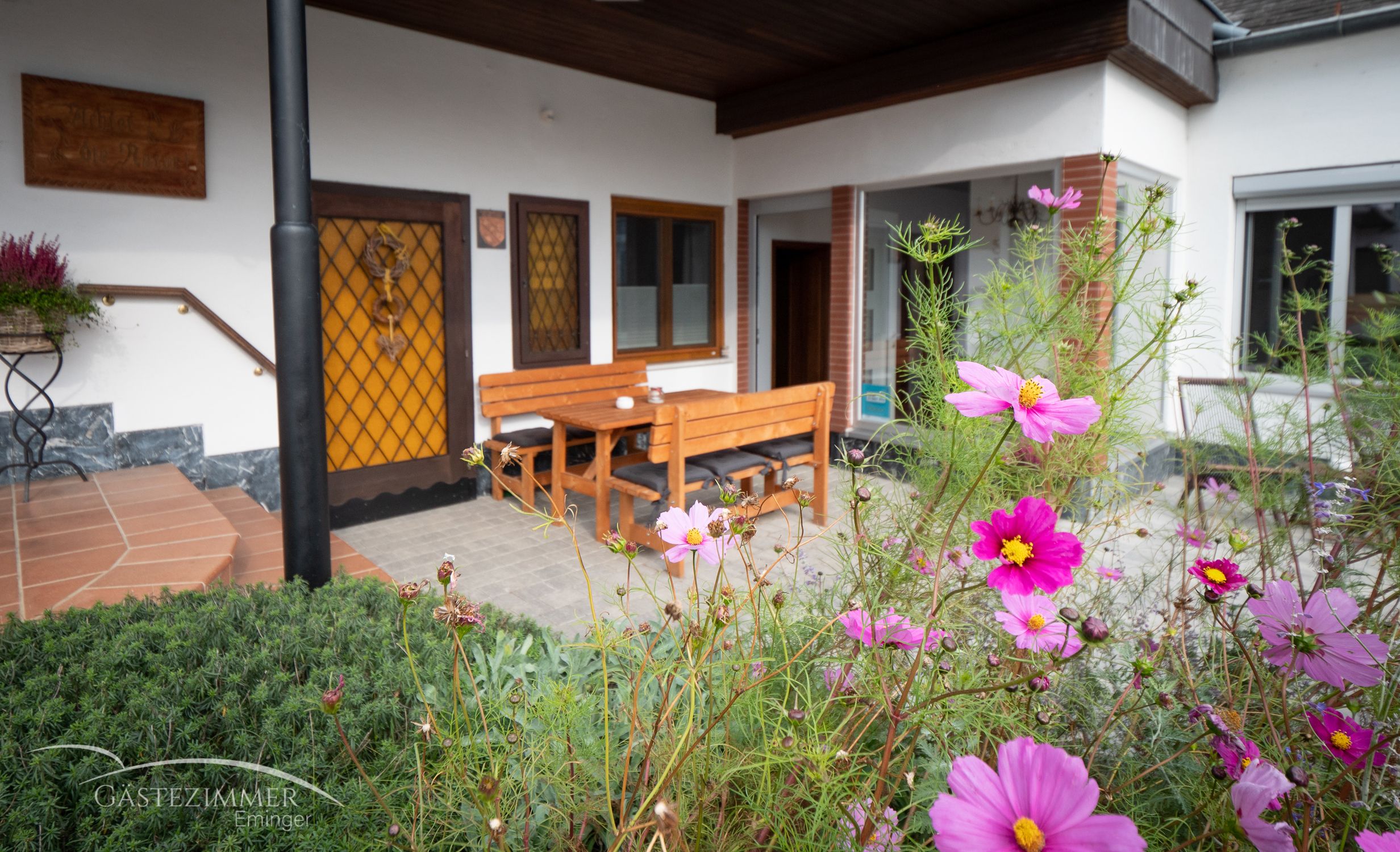 Terrasse mit Holzmöbeln und blühenden Blumen im Vordergrund.
