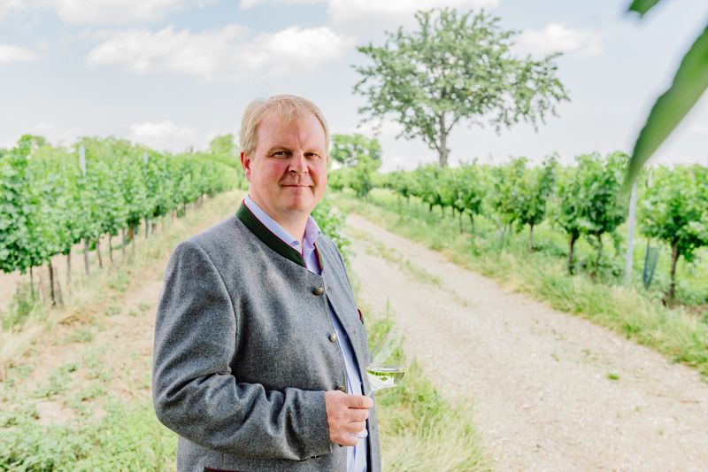 Man in traditional clothing with a wine glass in a vineyard.