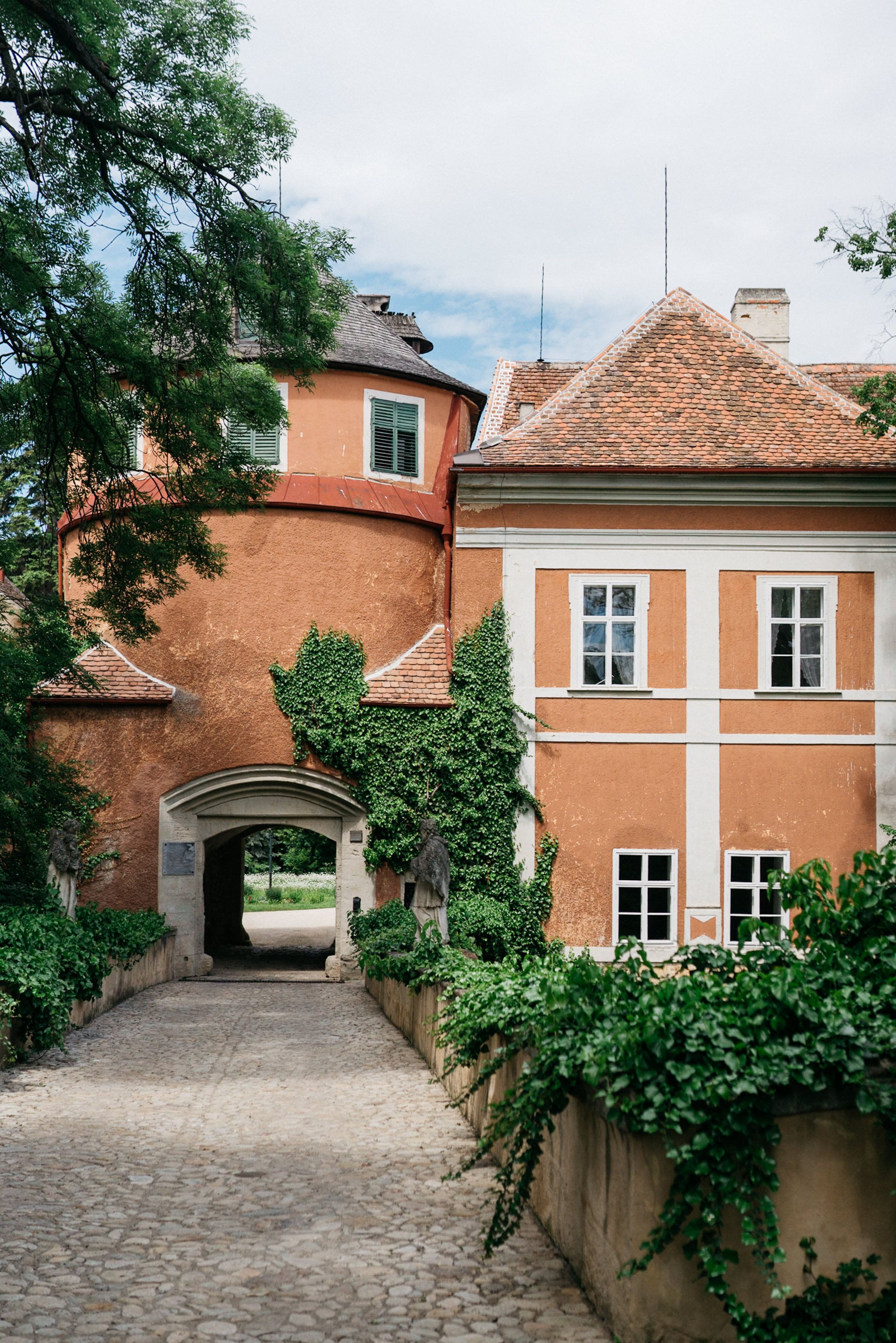 Vstupná brána do zámku Schrattenthal so zarastenou fasádou a vydláždenou cestou.