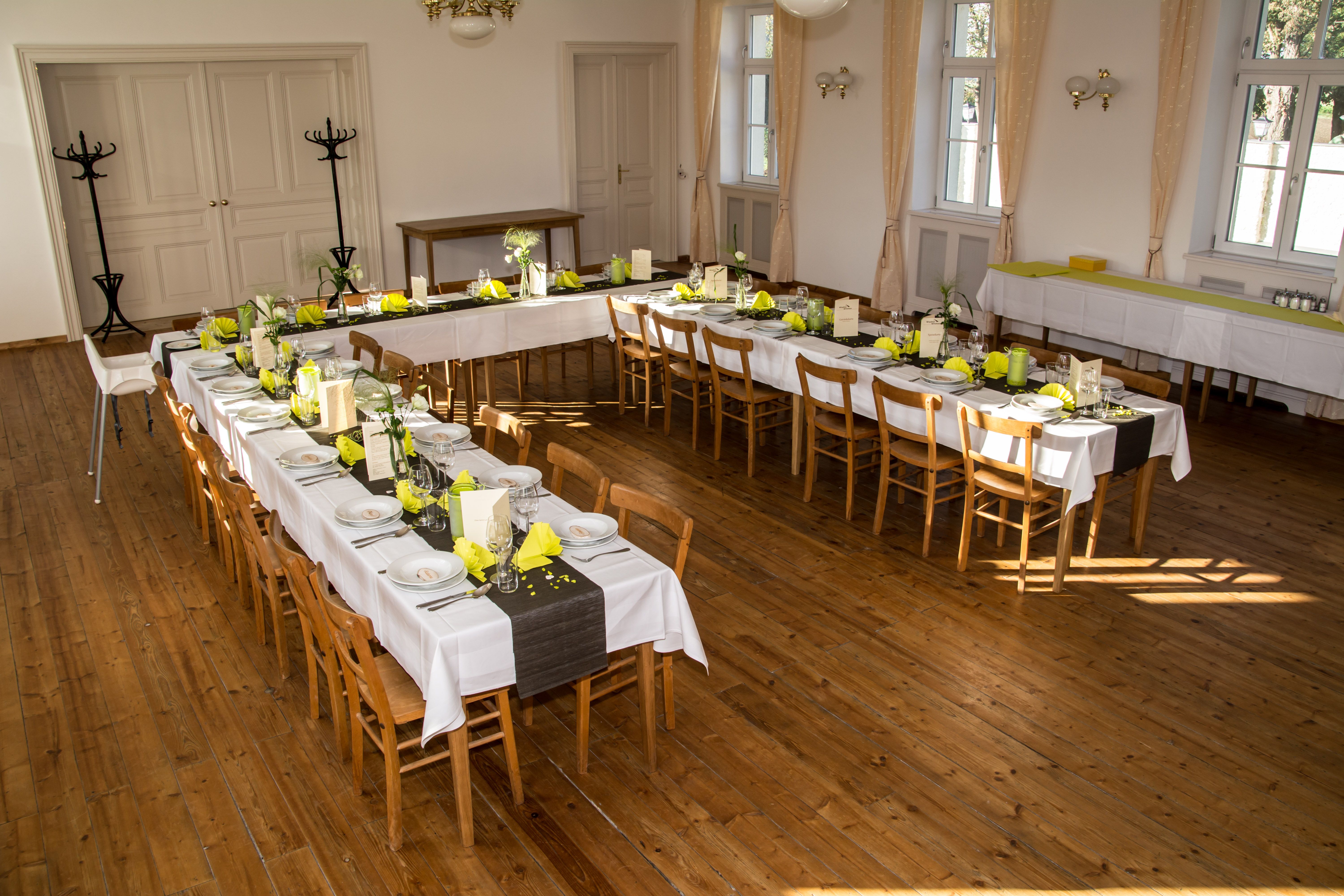 Festlich gedeckter Veranstaltungssaal mit langen Tafeln und gelben Servietten.
