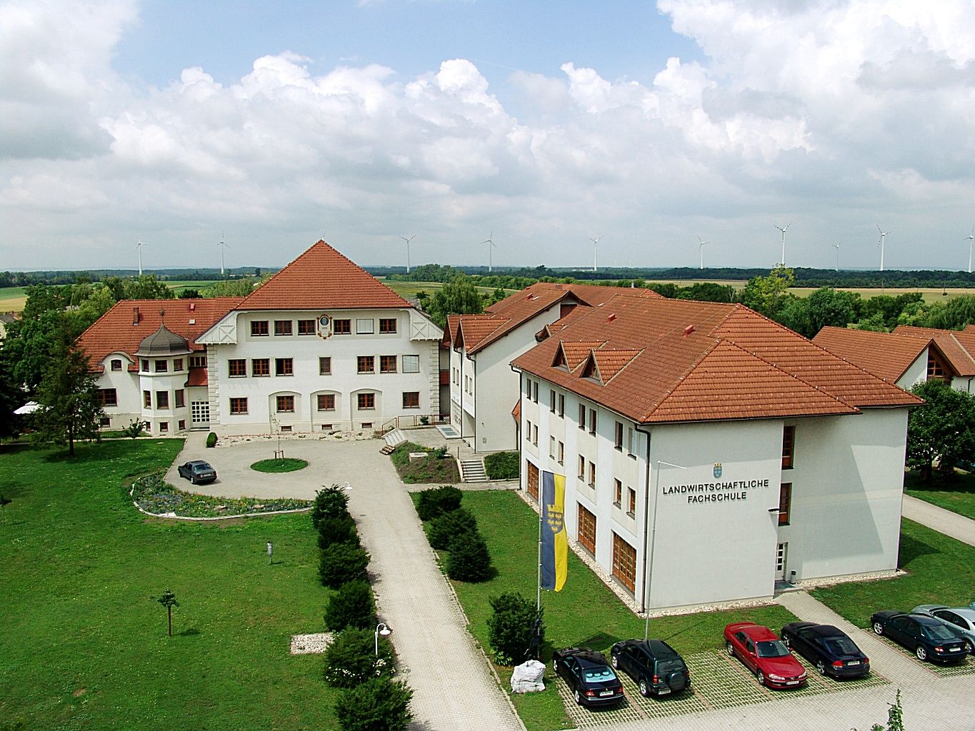 Luftaufnahme eines Schulgebäudekomplexes mit roten Dächern und umliegenden Grünflächen.