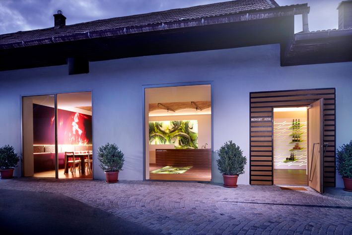 Außenansicht eines modernen Weinguts mit beleuchteten Fenstern und Pflanzen.