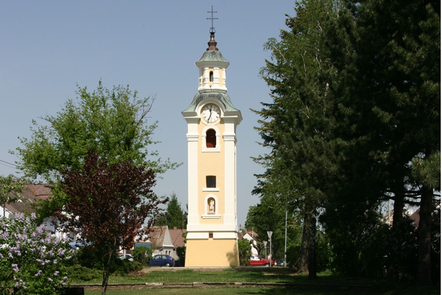 Gelber Kirchturm mit Uhr in Hohenau, umgeben von Bäumen.