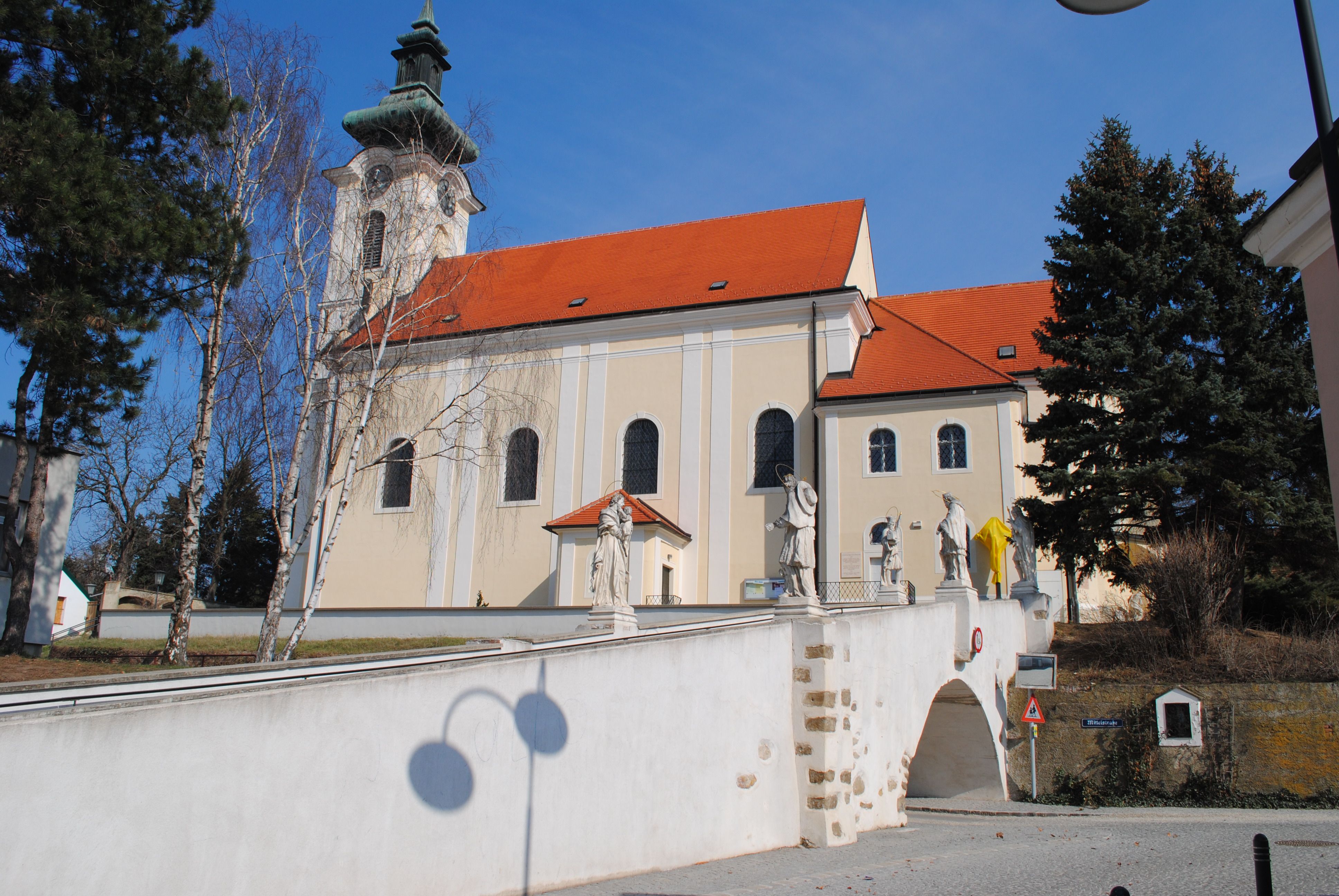 Farní kostel Wolkersdorf se sochami na mostě, modrá obloha.