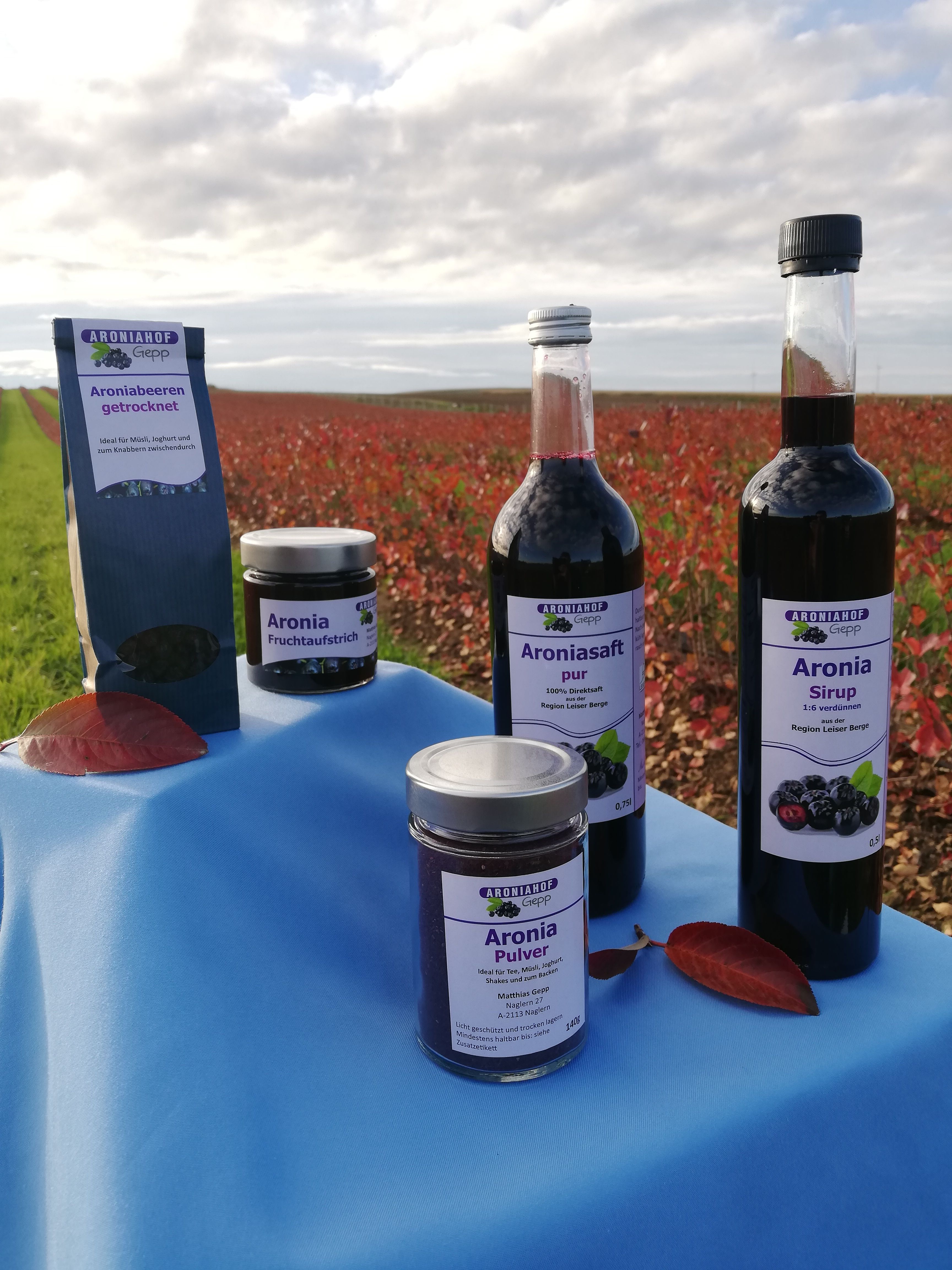 Produkte des Aroniahofs Gepp auf einem Tisch vor einem Feld.