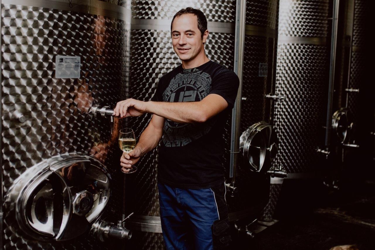 Man draws wine from a stainless steel tank in a wine cellar.
