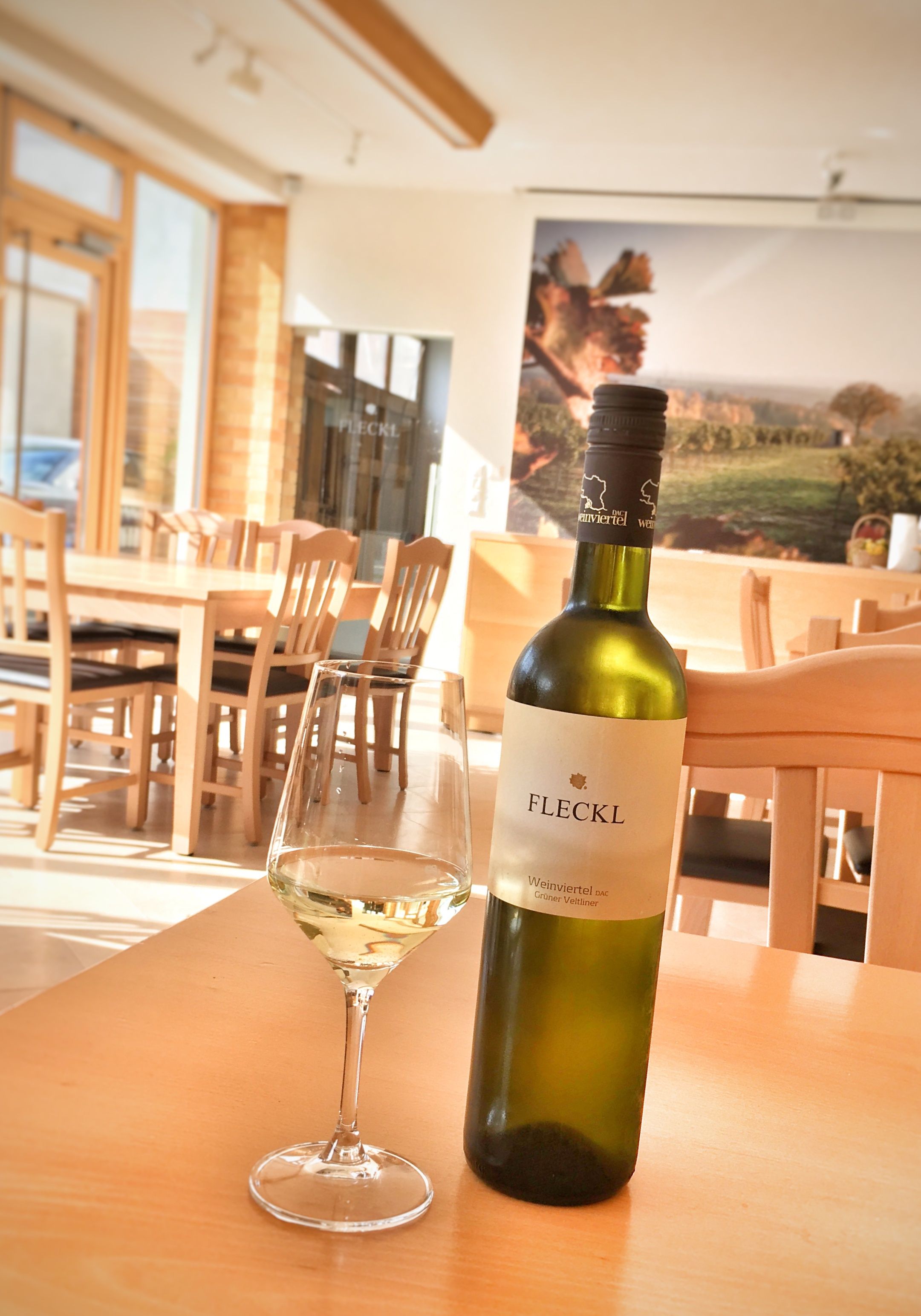 Eine Flasche Weißwein und ein gefülltes Weinglas auf einem Holztisch in einem Verkostungsraum.