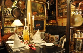 Gemütlich dekorierter Tisch in einem rustikalen Restaurant mit Kerzenleuchter, Bildern und antiken Gegenständen.