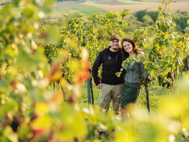 A man and a woman stand smiling in a vineyard.