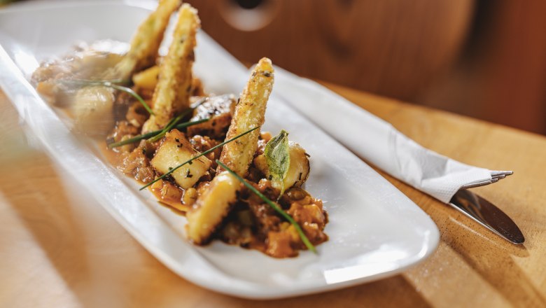 Gourmetgericht auf weißem Teller mit frittierten Gemüsesticks und Kräutern.