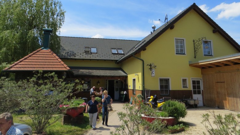 Ein gelbes Gasthaus mit grauem Dach und Garten im Vordergrund.