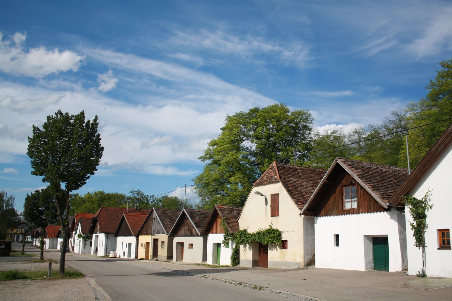 Reihe von traditionellen Weinkellern in einer Kellergasse mit blauem Himmel.
