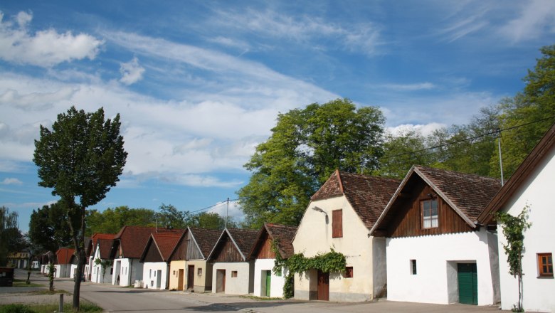 Reihe von traditionellen Weinkellern in einer Kellergasse mit blauem Himmel.