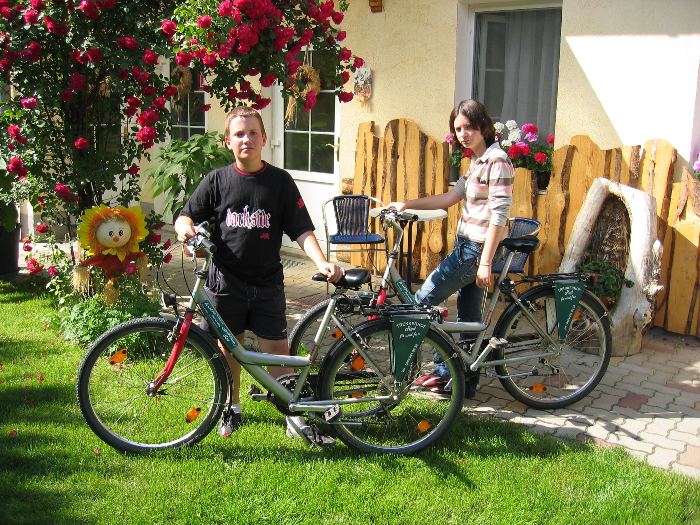 Zwei Personen mit Fahrrädern vor einem Haus mit Blumen und Holzdekoration.