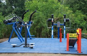 Outdoor-Fitnessgeräte auf blauen Bodenplatten im Freien.