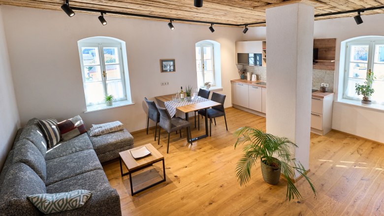Modernes Wohnzimmer mit Holzboden, grauem Sofa, Esstisch und Küche.