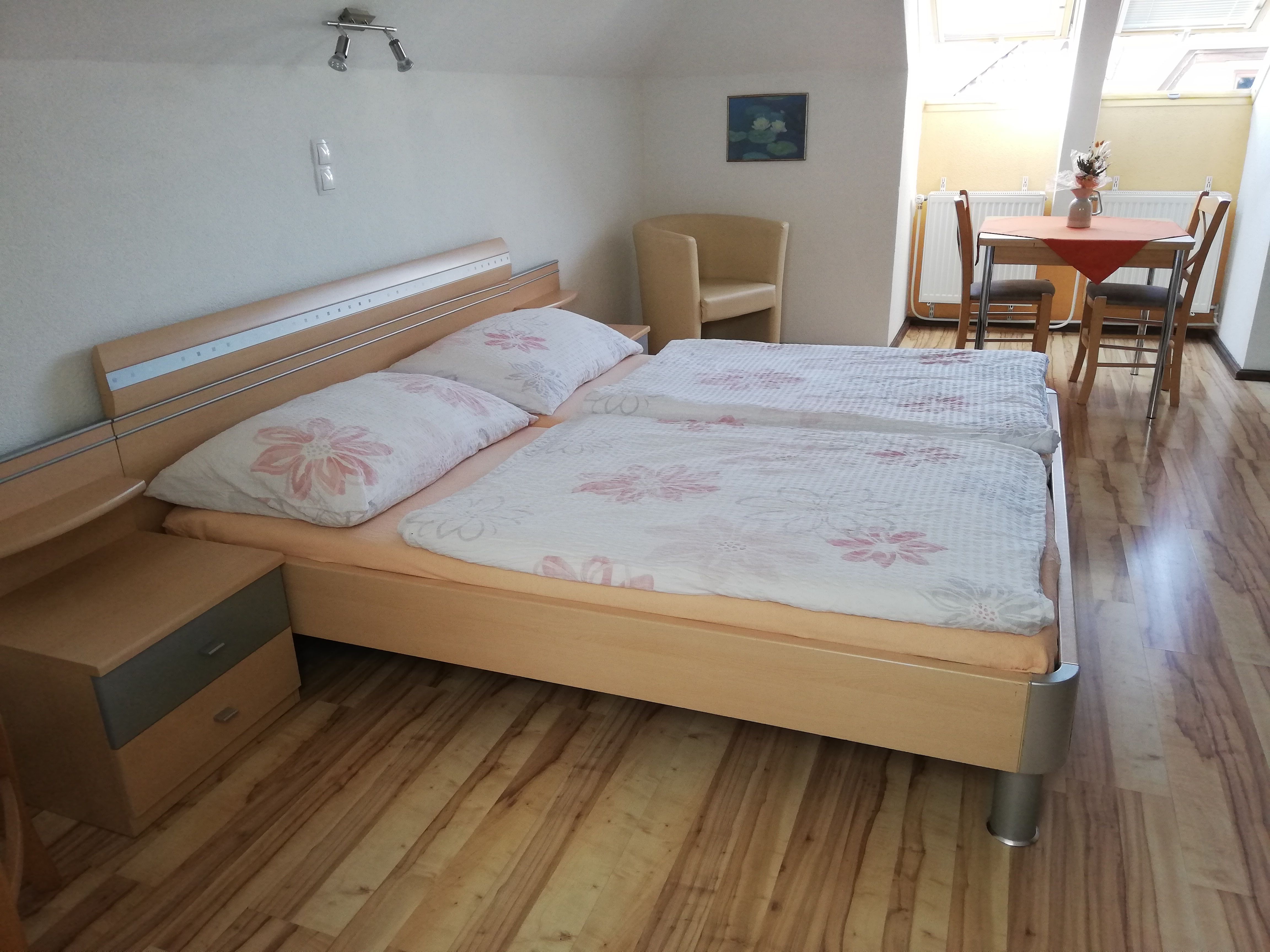 Ein gemütliches Doppelzimmer mit Holzboden, Doppelbett, Nachttisch, Tisch mit Stühlen und Dachfenster.