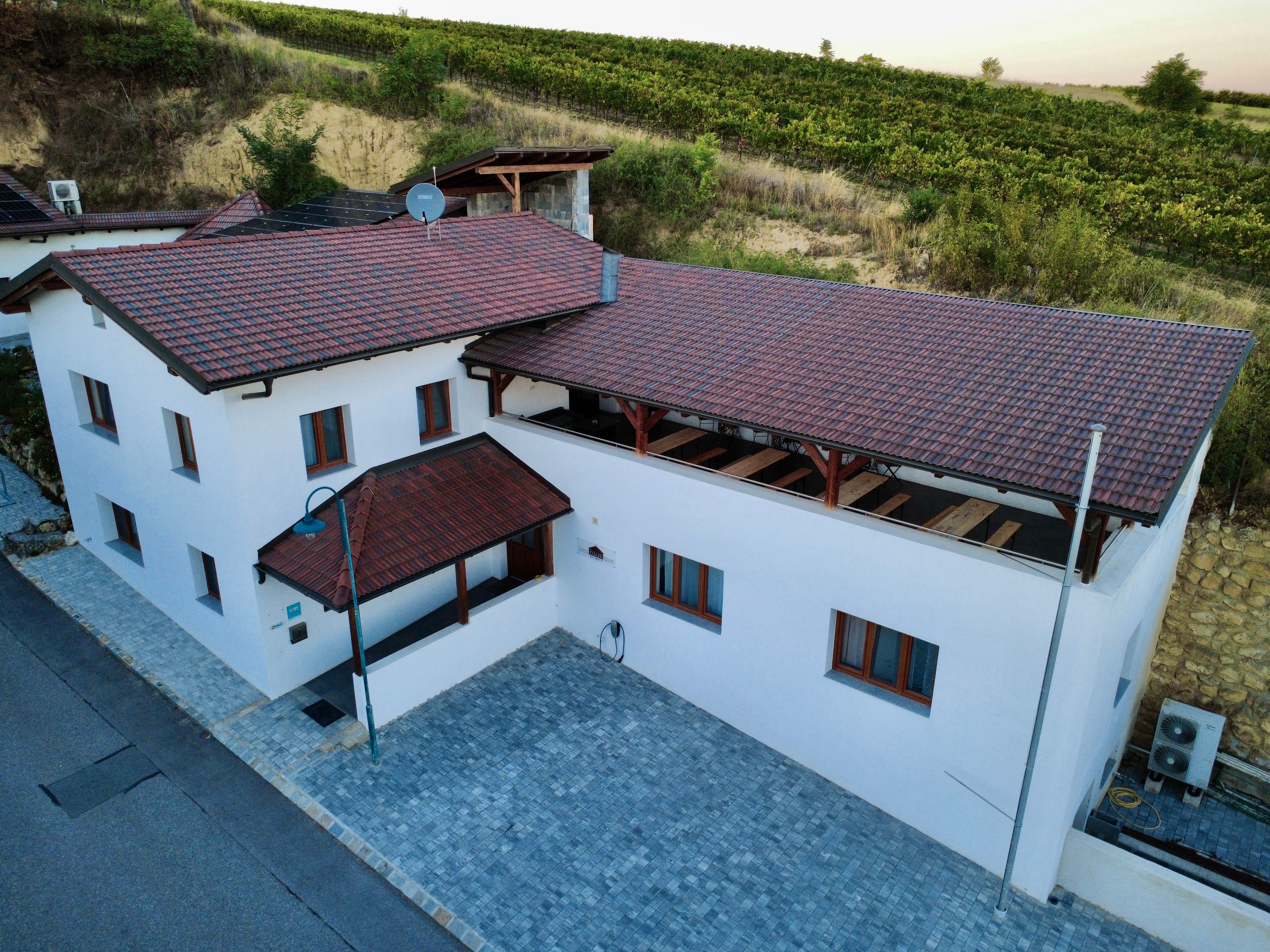 Frontansicht 7(c)Benjamin Sporr: Luftaufnahme eines weißen Hauses mit rotem Ziegeldach, Innenhof und Terrasse vor einem Weinberg.