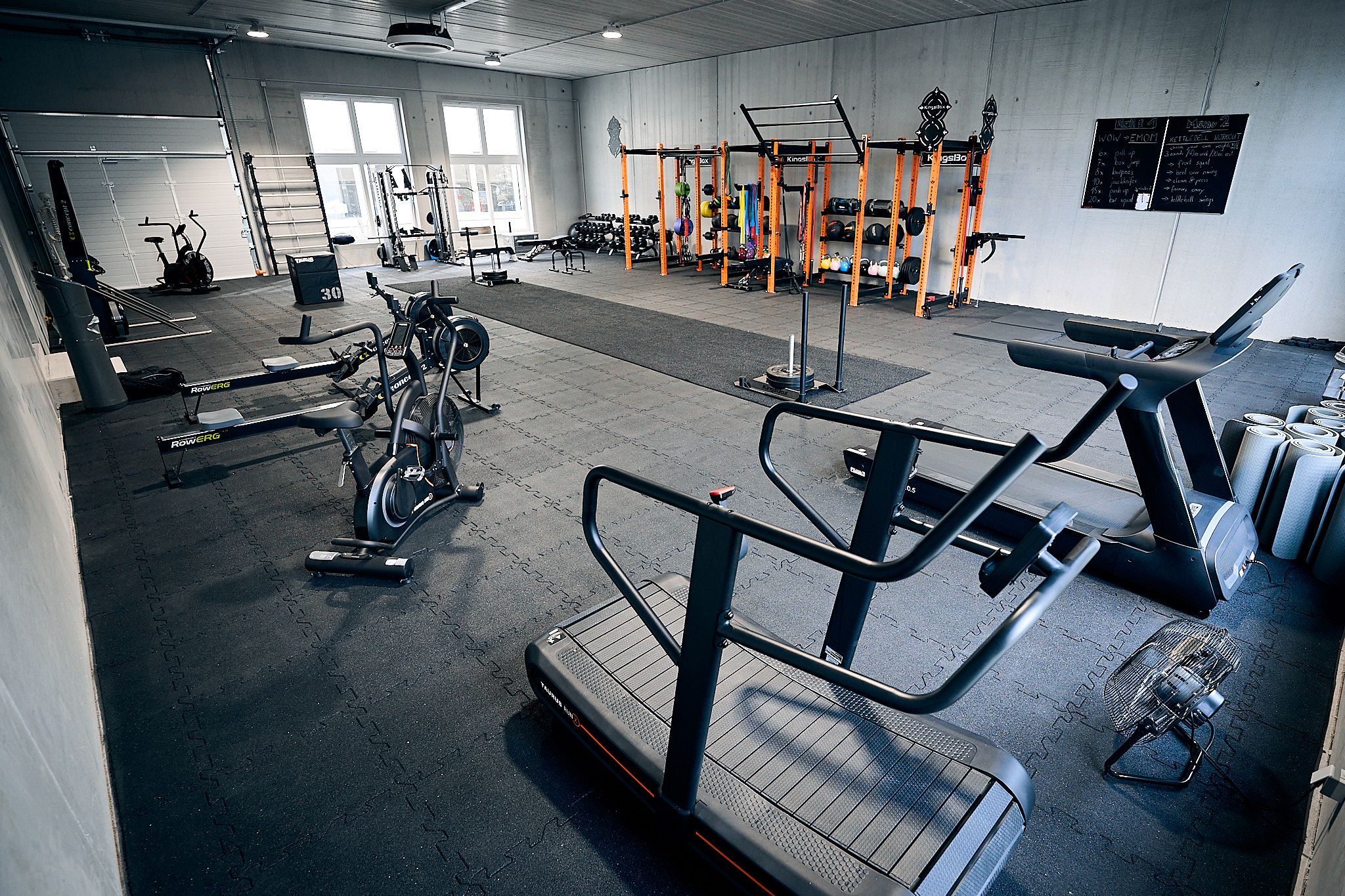 Interior view of a fitness studio with various training equipment such as treadmills, bicycles and dumbbells.