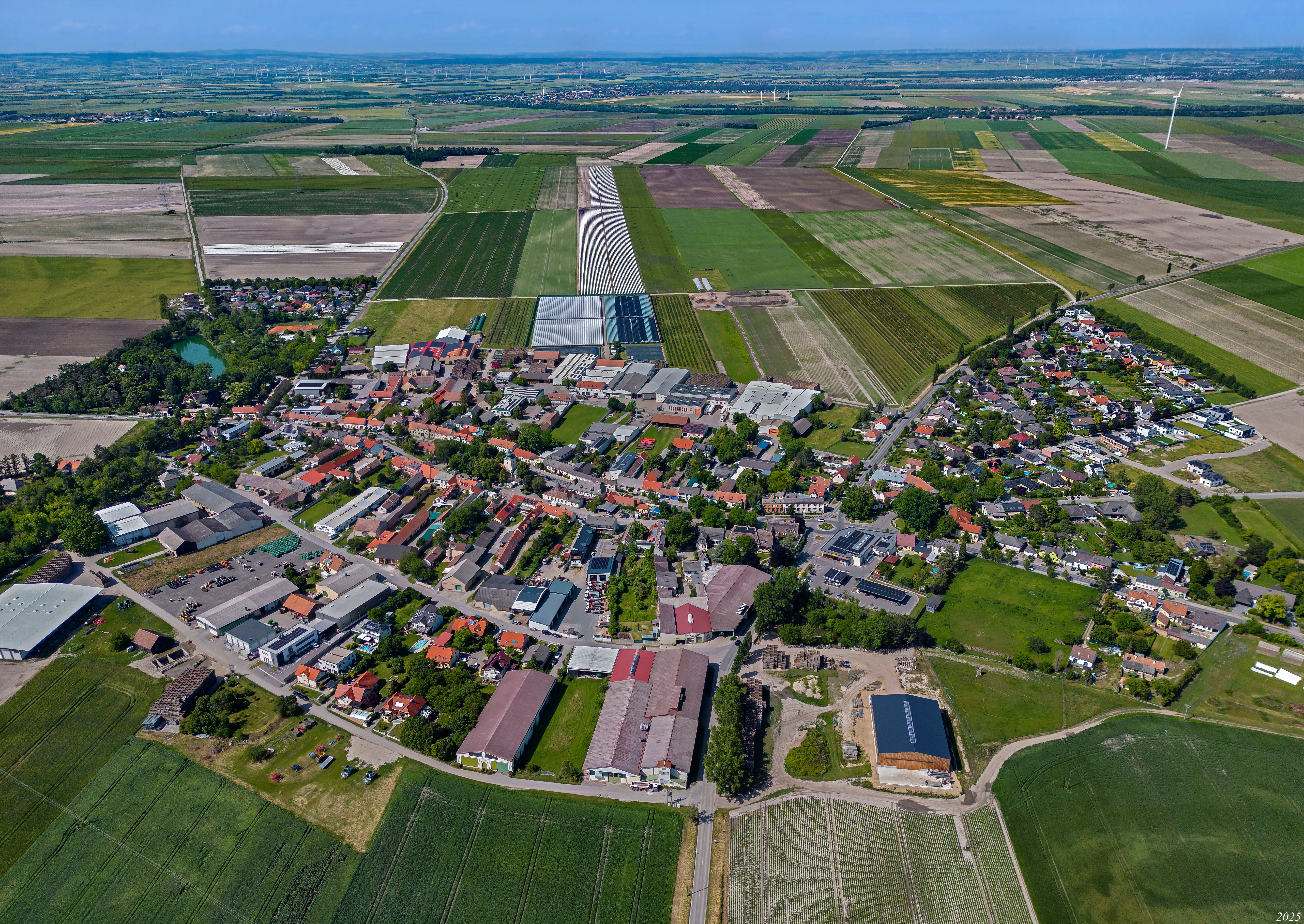 Luftbild von Raasdorf mit Ortskern, Feldern, Gewächshäusern und Windrädern in der Umgebung.